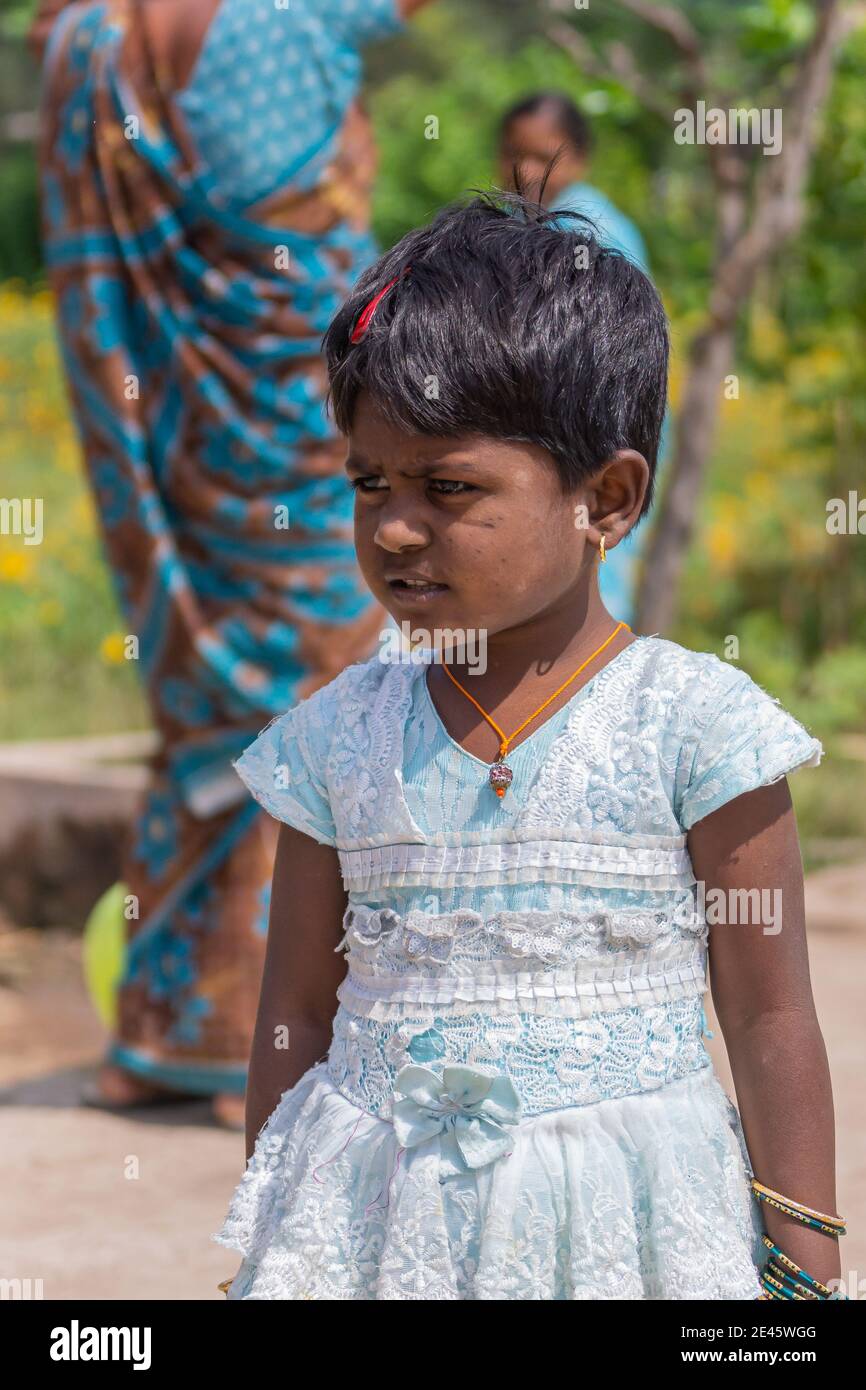 Lakundi, Karnataka, India - November 6, 2013: Closeup of little girl in white-blue dress, short black hair, earrings and other jewelry. Faded backgrou Stock Photo