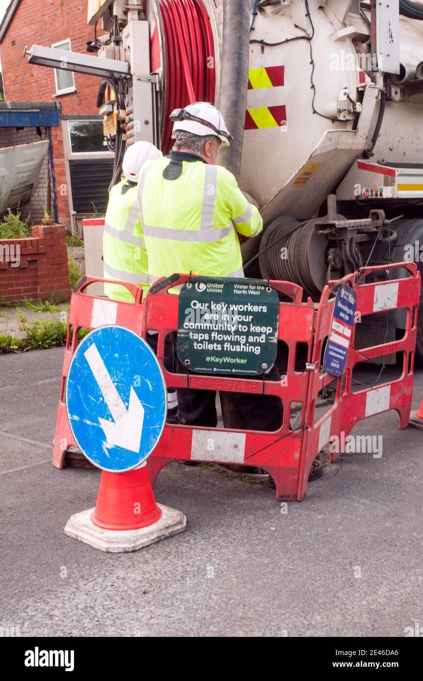Workmen operating controls on rear of sewer cleaning vehicle with safety barriers in place and Key workers sign during Covid 19 Pandemic Stock Photo