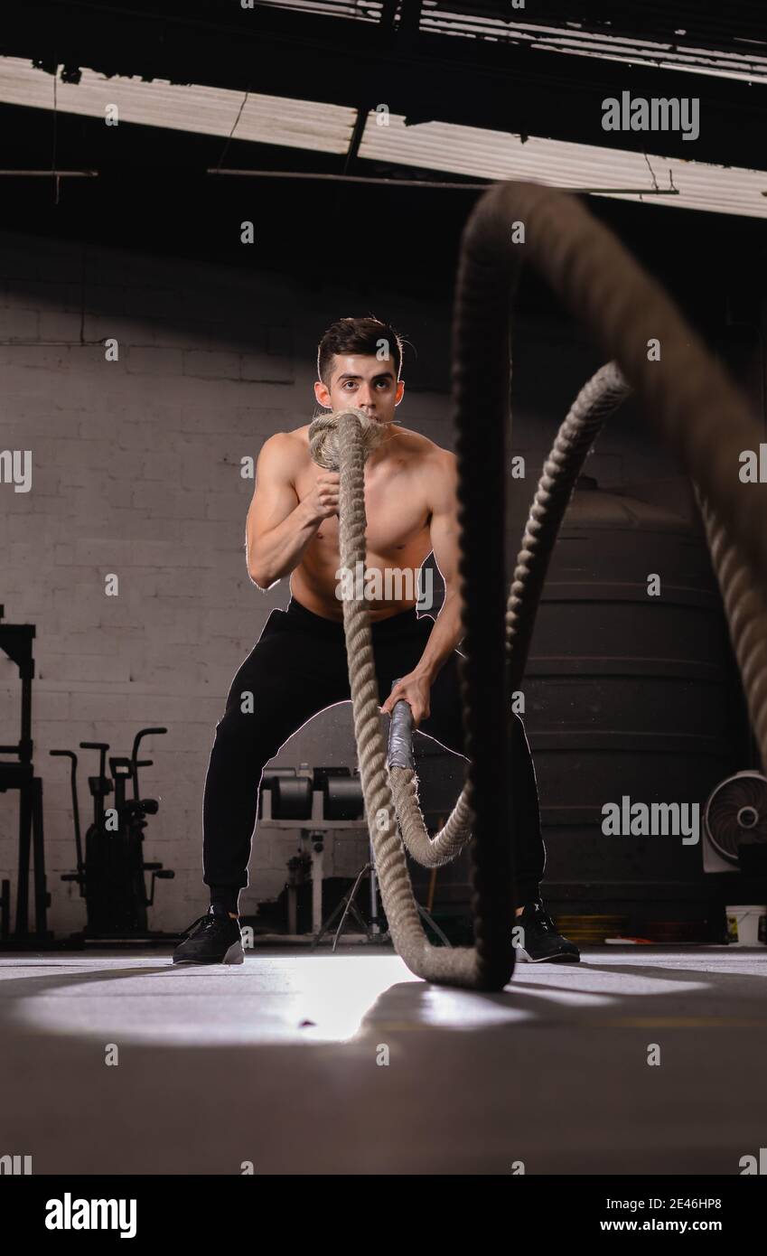 Young fit sportsman doing crossfit exercise with battle ropes in the ...