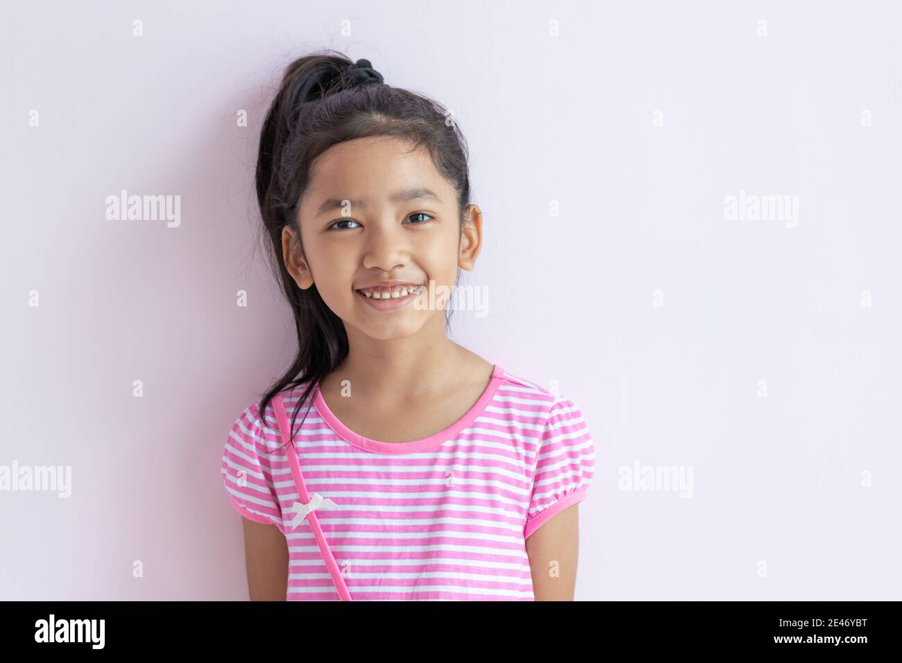 Portrait of an Asian little girl wearing a pink and white striped dress. The child tied up black hair and smiled with happiness. Stock Photo