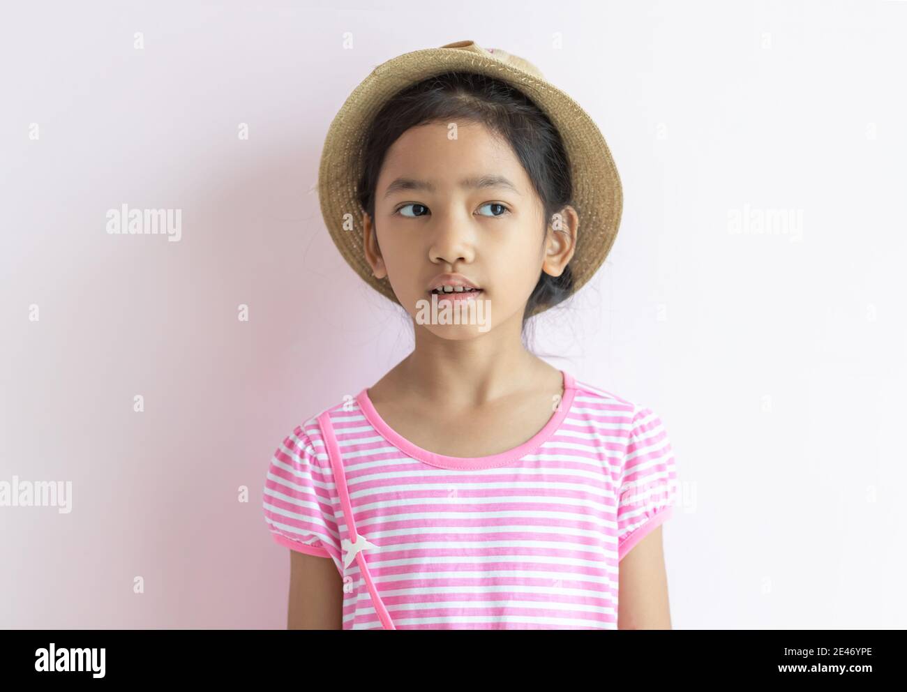 Portrait of an Asian kid wearing a pink and white striped dress. The girl wore a hat and looking to her side. Stock Photo