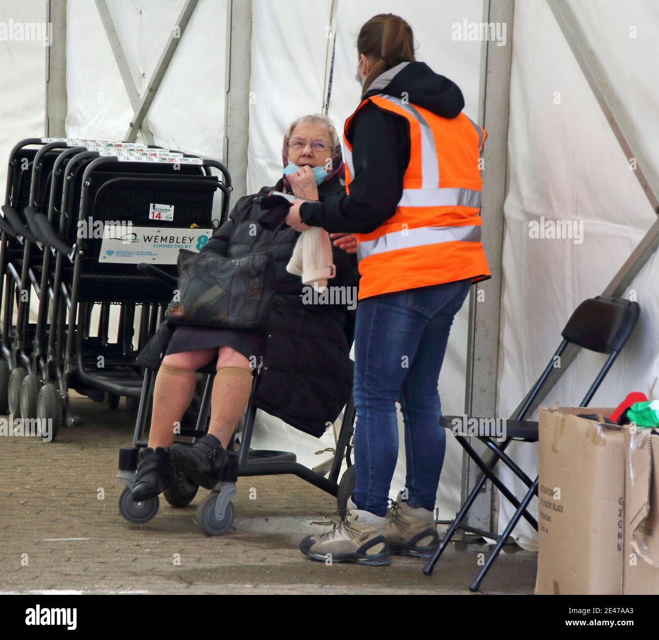 London, UK. 21st Jan, 2021. A steward attends to an elderly woman inside the vaccination centre entrance.A steady stream of elderly people with pre-booked appointments at the new Covid-19 Vaccination hub at the Olympic Office Centre, near London's Wembley Stadium. It is one of 10 new large scale Vaccination centres opened this week, to join the seven already in use across the country. So far 4.9 million people across the UK have received the first dose of vaccine and the government aims for that number to rise to 15 million by 15 February. Credit: SOPA Images Limited/Alamy Live News Stock Photo