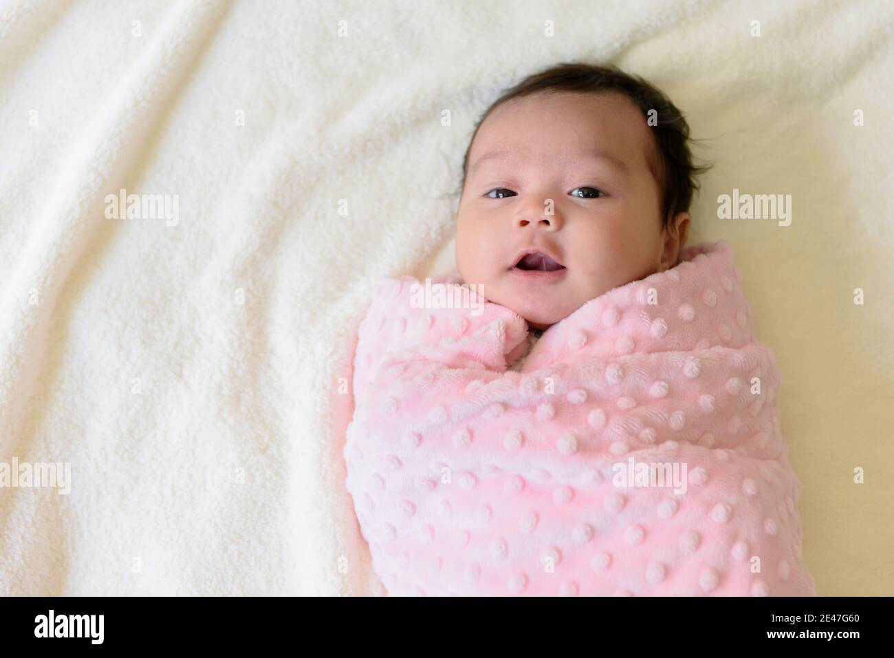 Top view of a cute Asian baby girl wrapped in a pink cloth on the bed Stock Photo