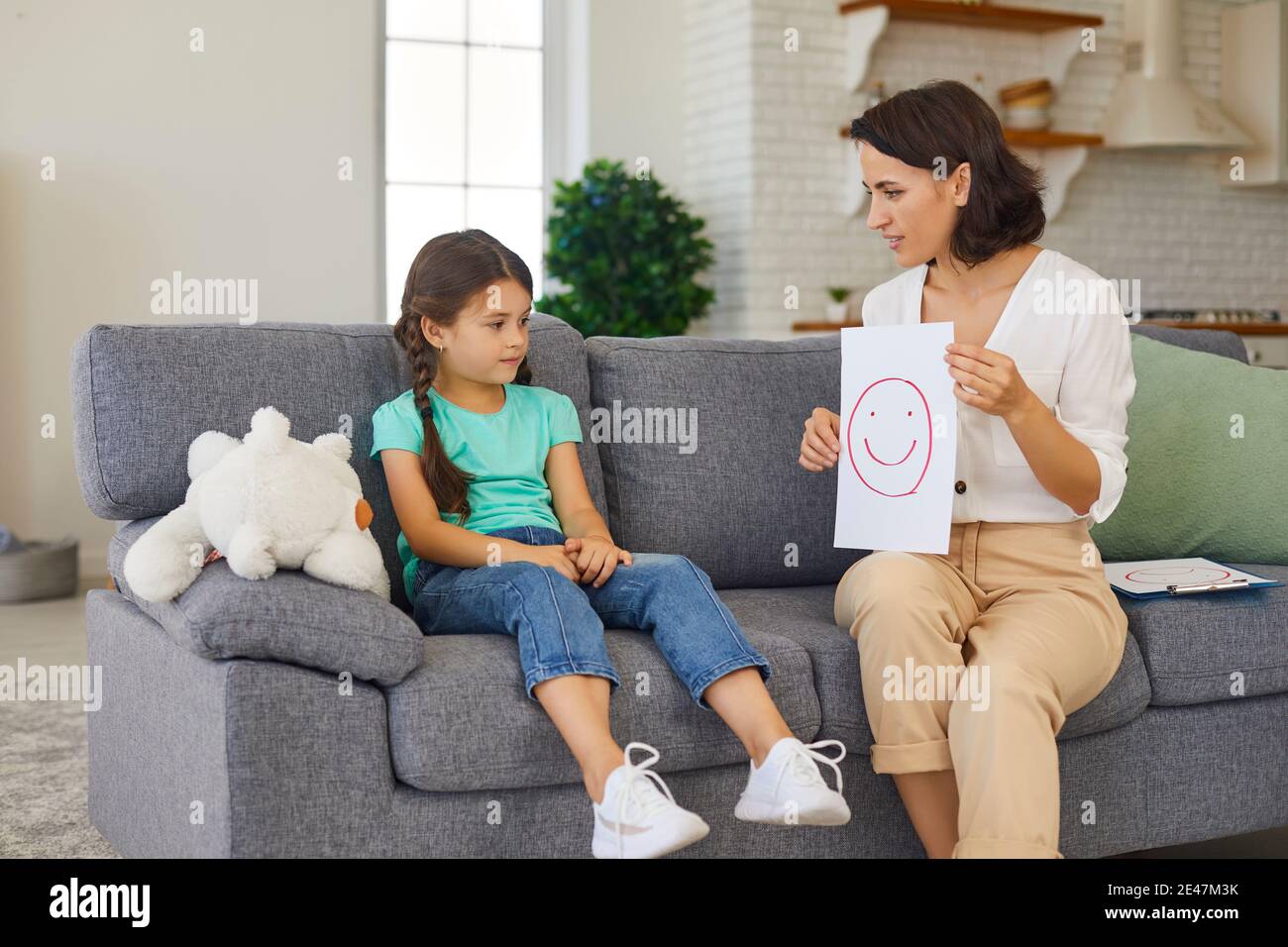 Professional female psychologist shows a little girl a picture of a cheerful face. Stock Photo