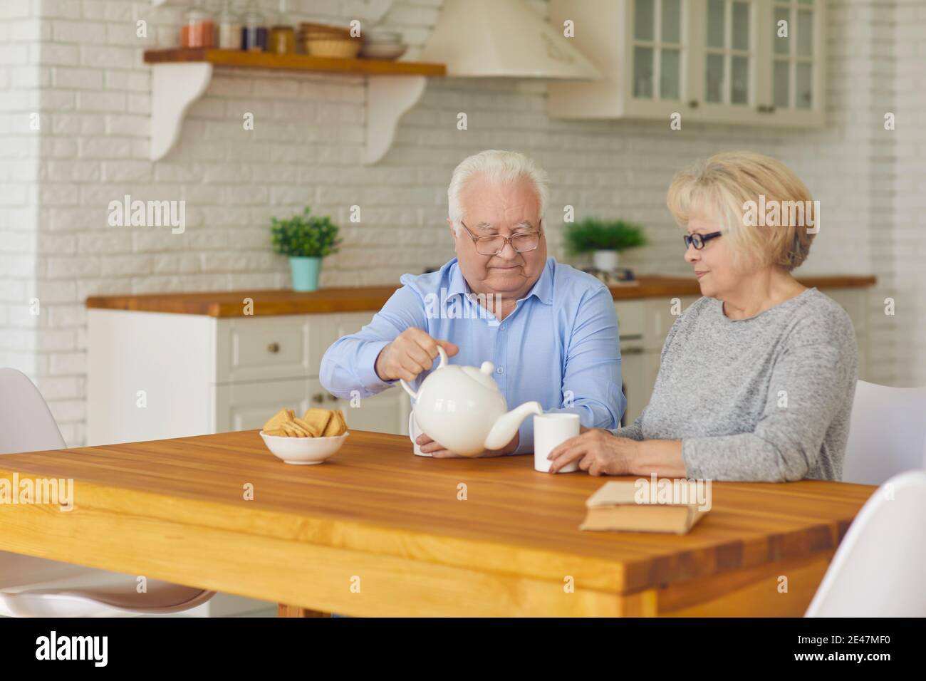 Happy senior couple grandparents sitting in kitchen, drinking tea with biscuits Stock Photo