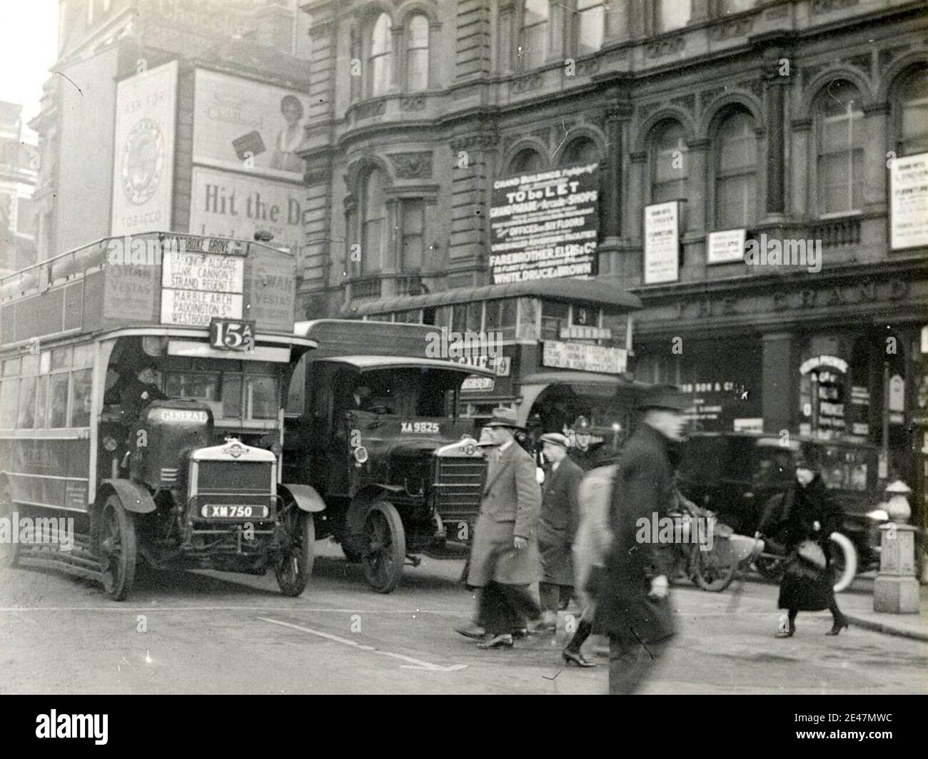 London traffic at the west end of the Strand heading west, about to enter Trafalgar Square. In view are two buses sandwiching a lorry, plus a motorcylce with sidecar and a car, perhaps a London Taxi?. The buses are AEC NS-Type double-deckers of the London General Omnibus Company Stock Photo
