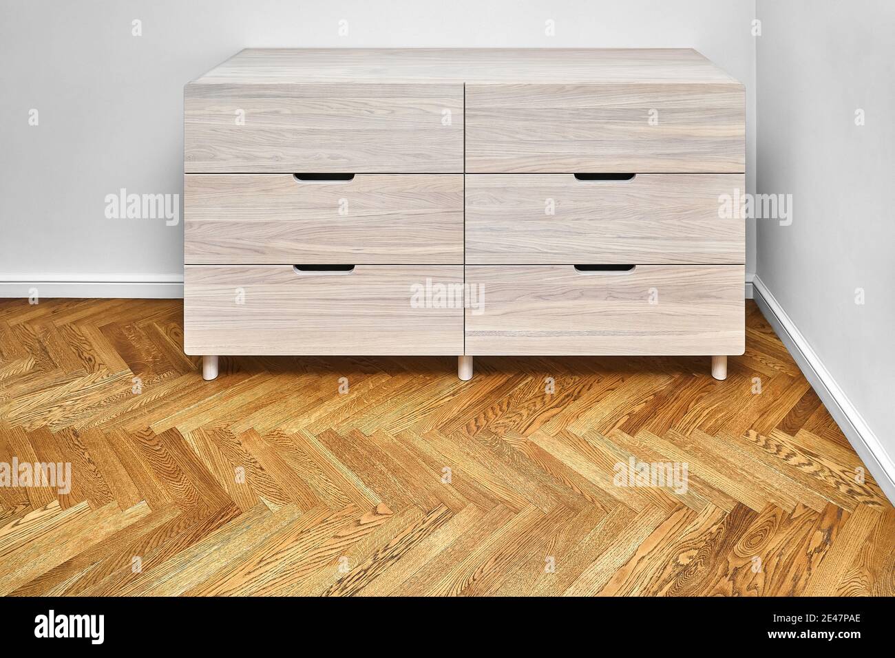 Elegant chest of drawers made with bleached solid oak timber with finger pull drawers stands on wood block parquet floor in light room. Axonometric vi Stock Photo