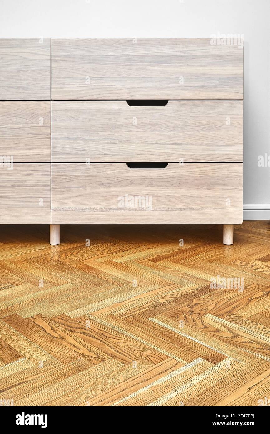 Stylish chest of drawers made with bleached solid oak timber with finger pull sliding stands on parquet floor near white wall Stock Photo