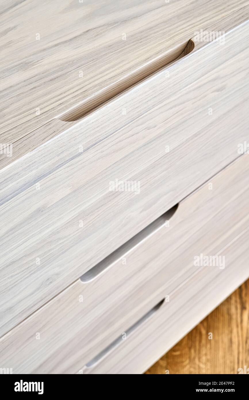 Contemporary chest of drawers made with bleached solid oak wood with finger pull drawers stands on floor in light room extreme closeup Stock Photo