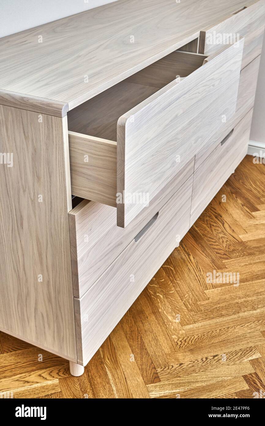 Contemporary chest of drawers made with bleached solid oak timber with open finger pull drawer stands on parquet floor in room closeup Stock Photo