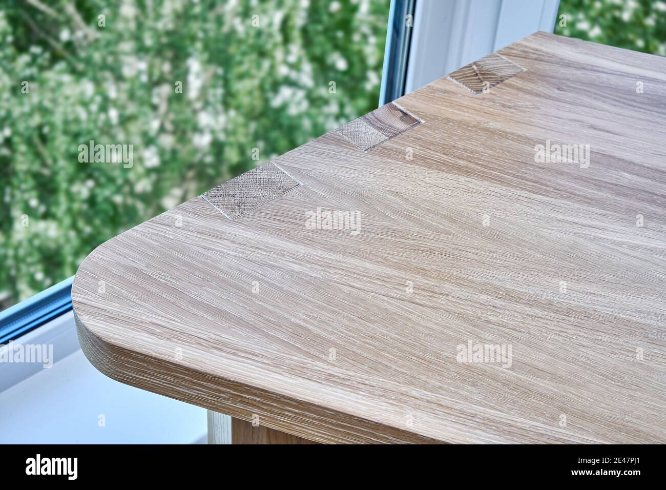 Elegant writing desk made with bleached solid oak timber stands on a cork floor against of trees outside the window in light room, close upper view Stock Photo