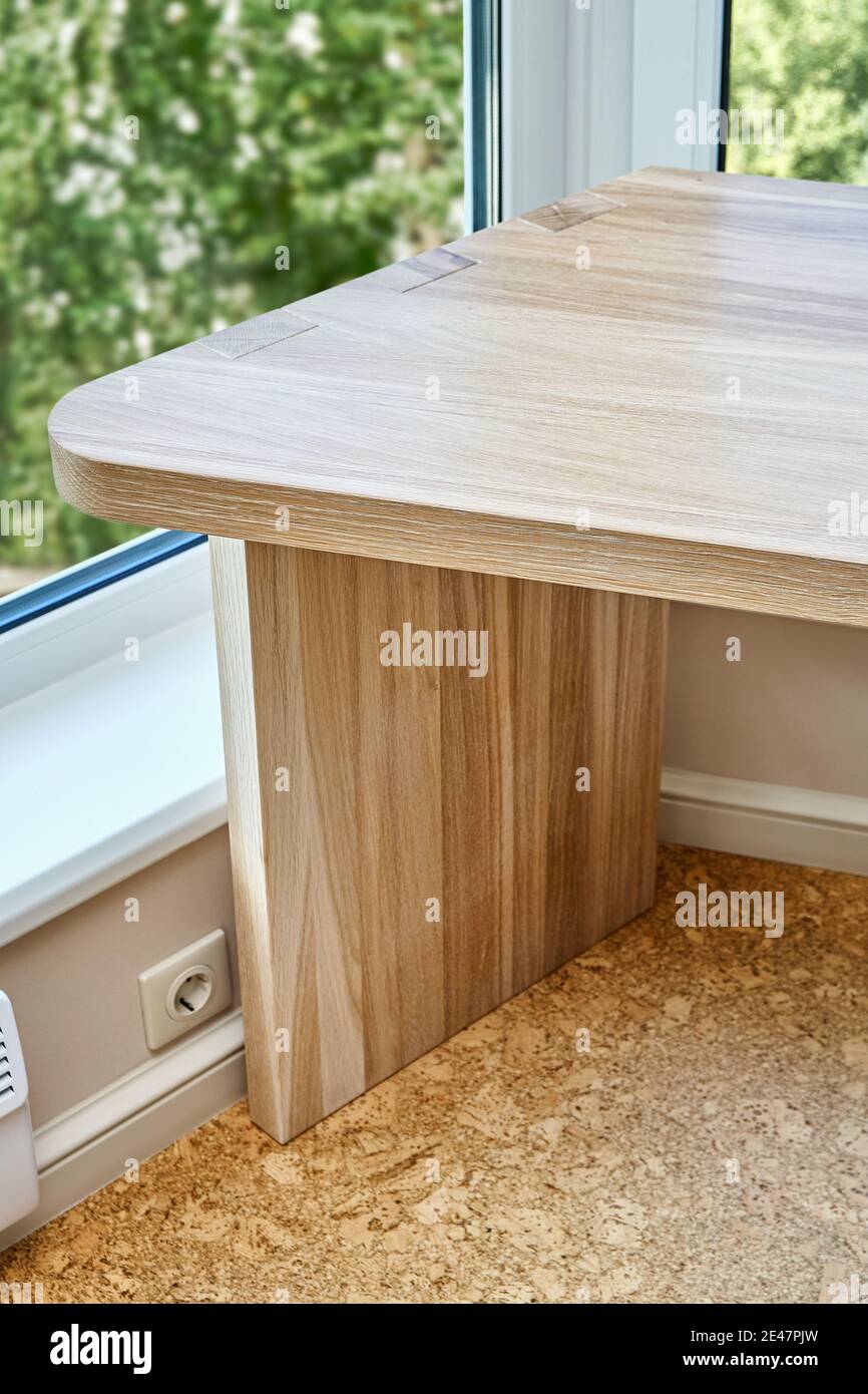 Elegant writing desk made with bleached solid oak timber stands on a cork floor against of trees outside the window in light room, upper view Stock Photo