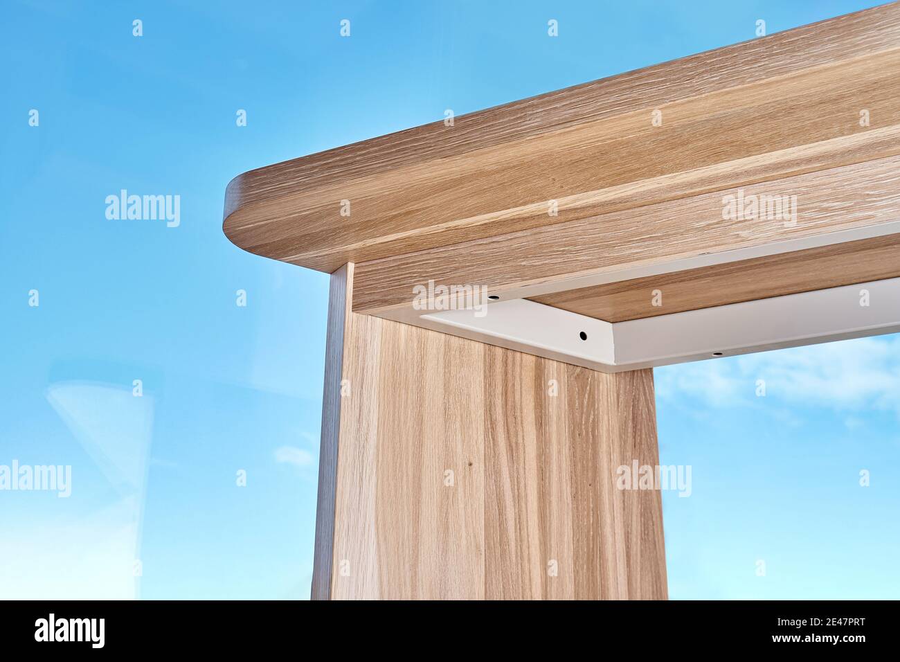 Elegant writing desk made with bleached solid oak timber stands on a cork floor against the sky outside the window in light room, close bottom view Stock Photo