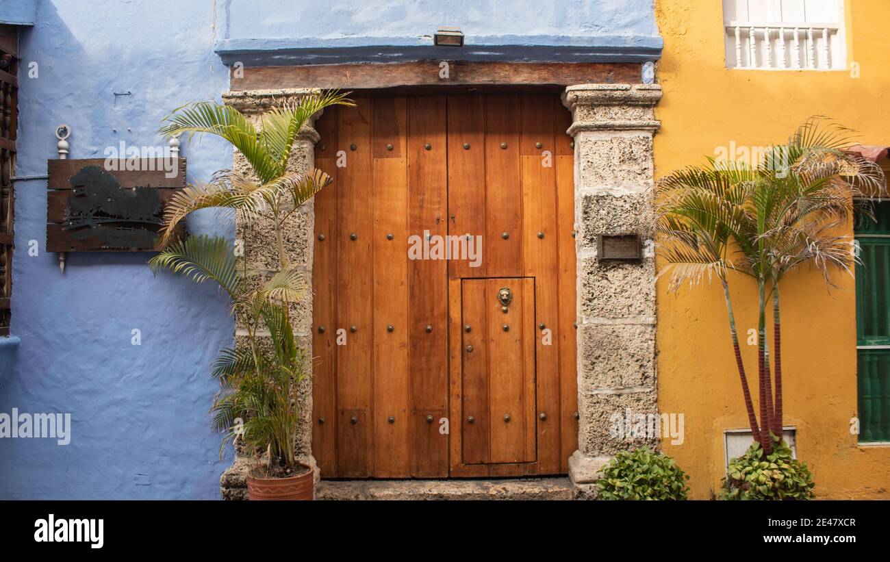 House with colorful exterior walls and a big wooden entry door with two potted palm trees next to it Stock Photo