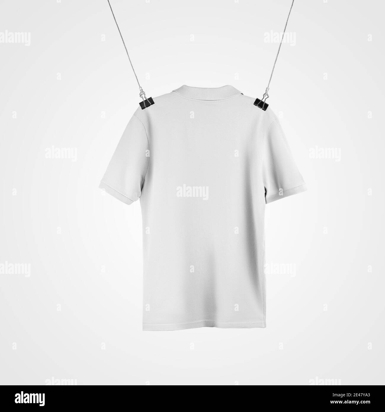 Template of a white textured T-shirt hanging from a rope by a hanger, mens polo isolated on background, back view.Mockup of casual clothes for design Stock Photo