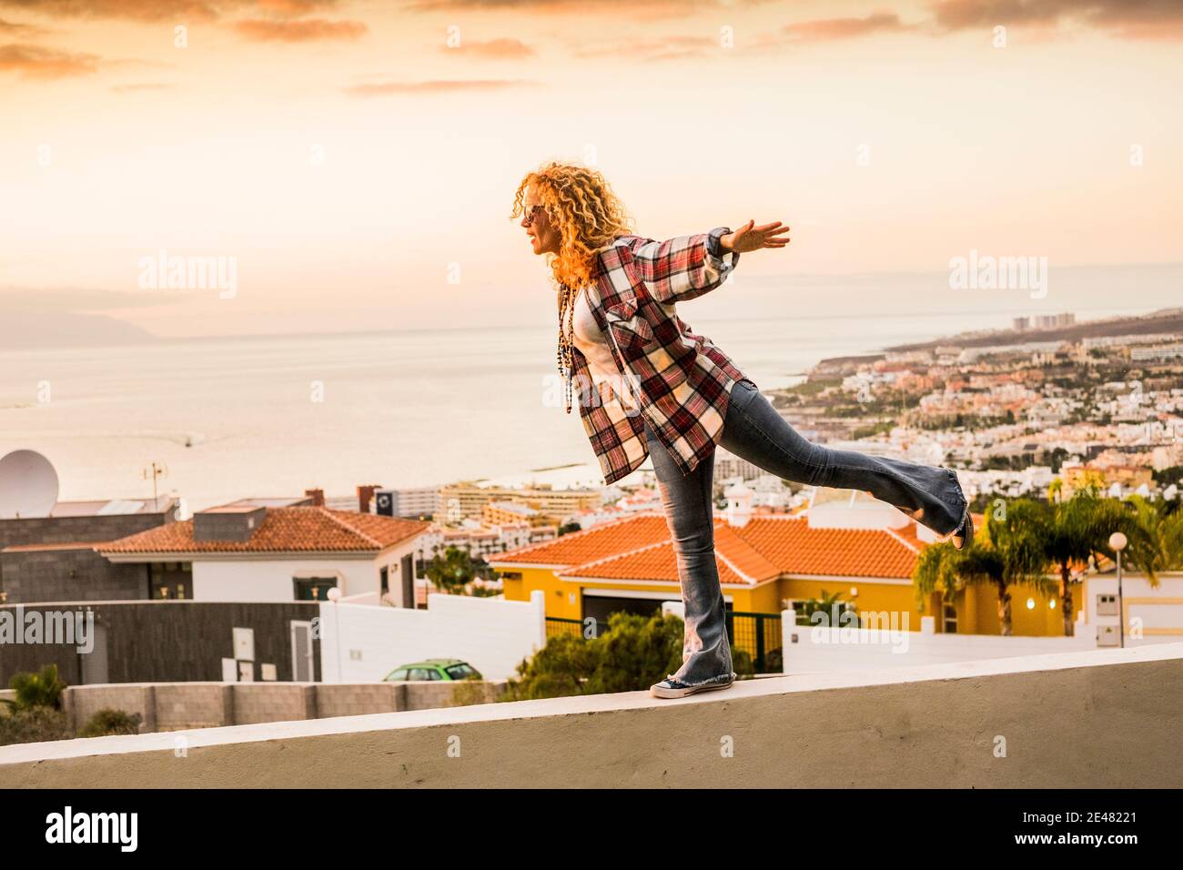 Happiness and freedom concept for independent young beautiful woman walking balanced on a wall with city and sea coast in background - summer holiday Stock Photo