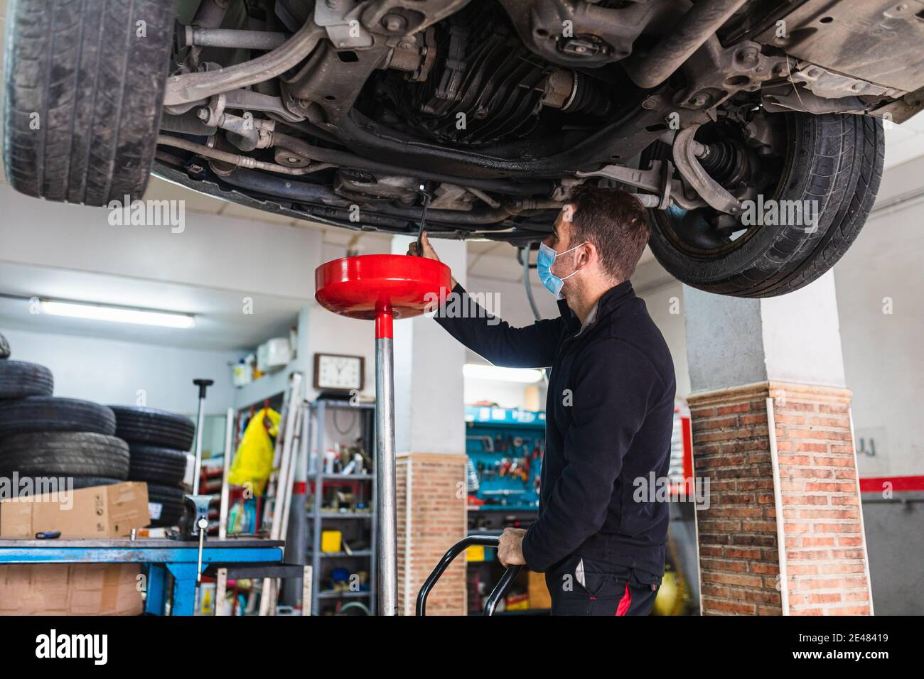 Mechanic with mask changing the oil of the car. Stock Photo