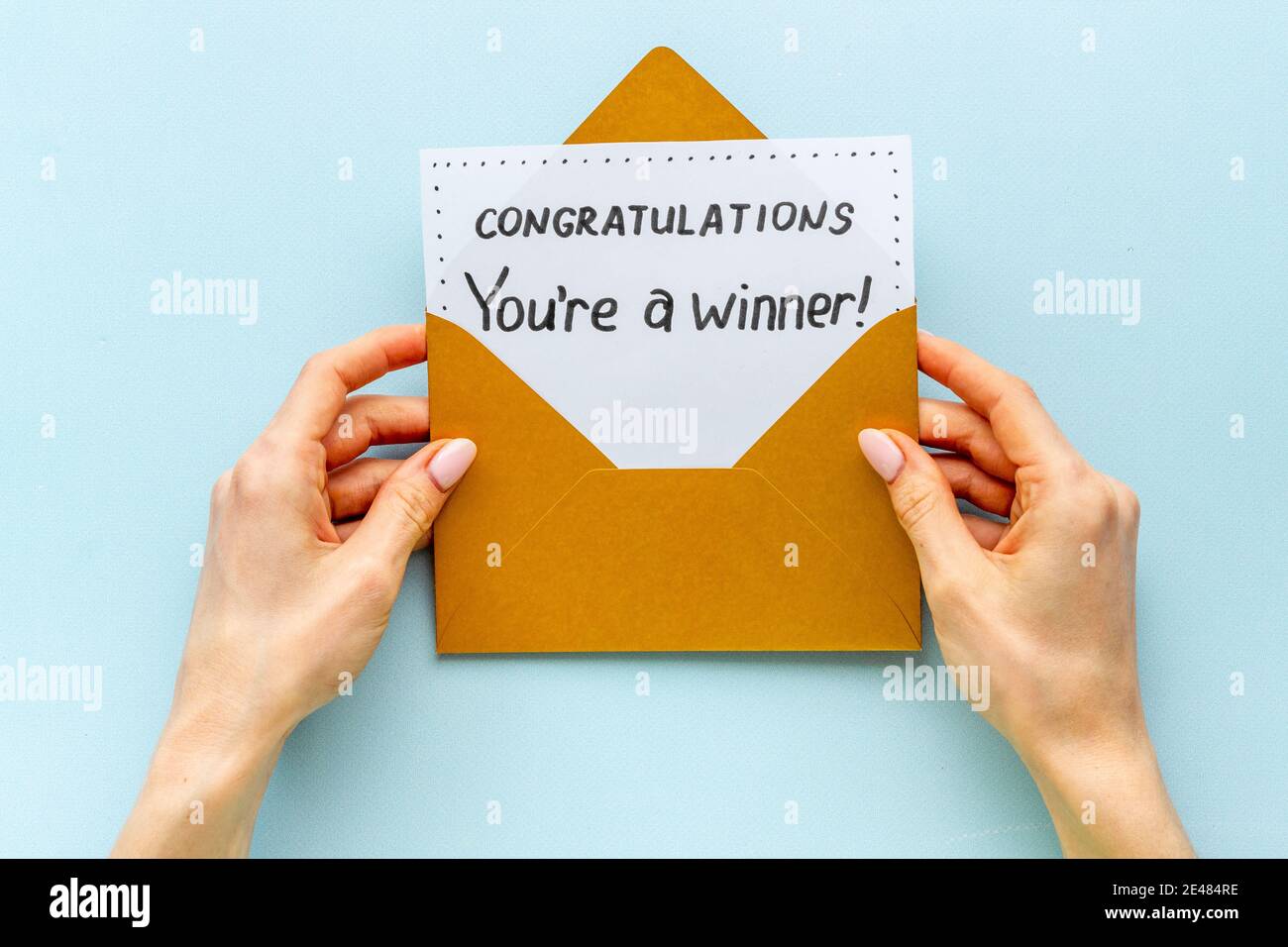 Hands holding award congratulation card in golden envelope. Text You're a winner in letter Stock Photo