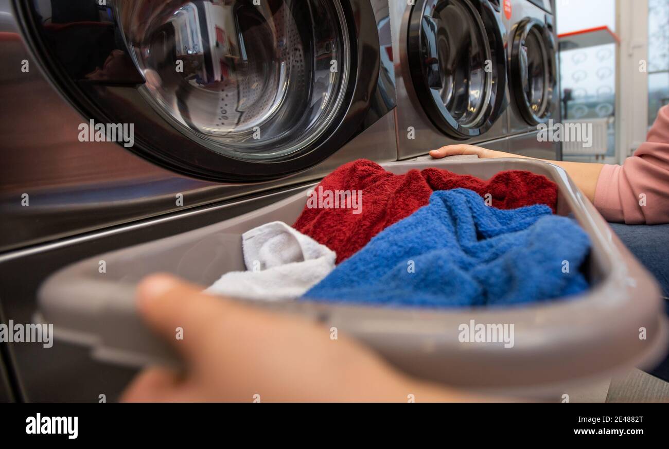 Young woman with full box of dirty clothes by the washing machine in the laundry room Stock Photo