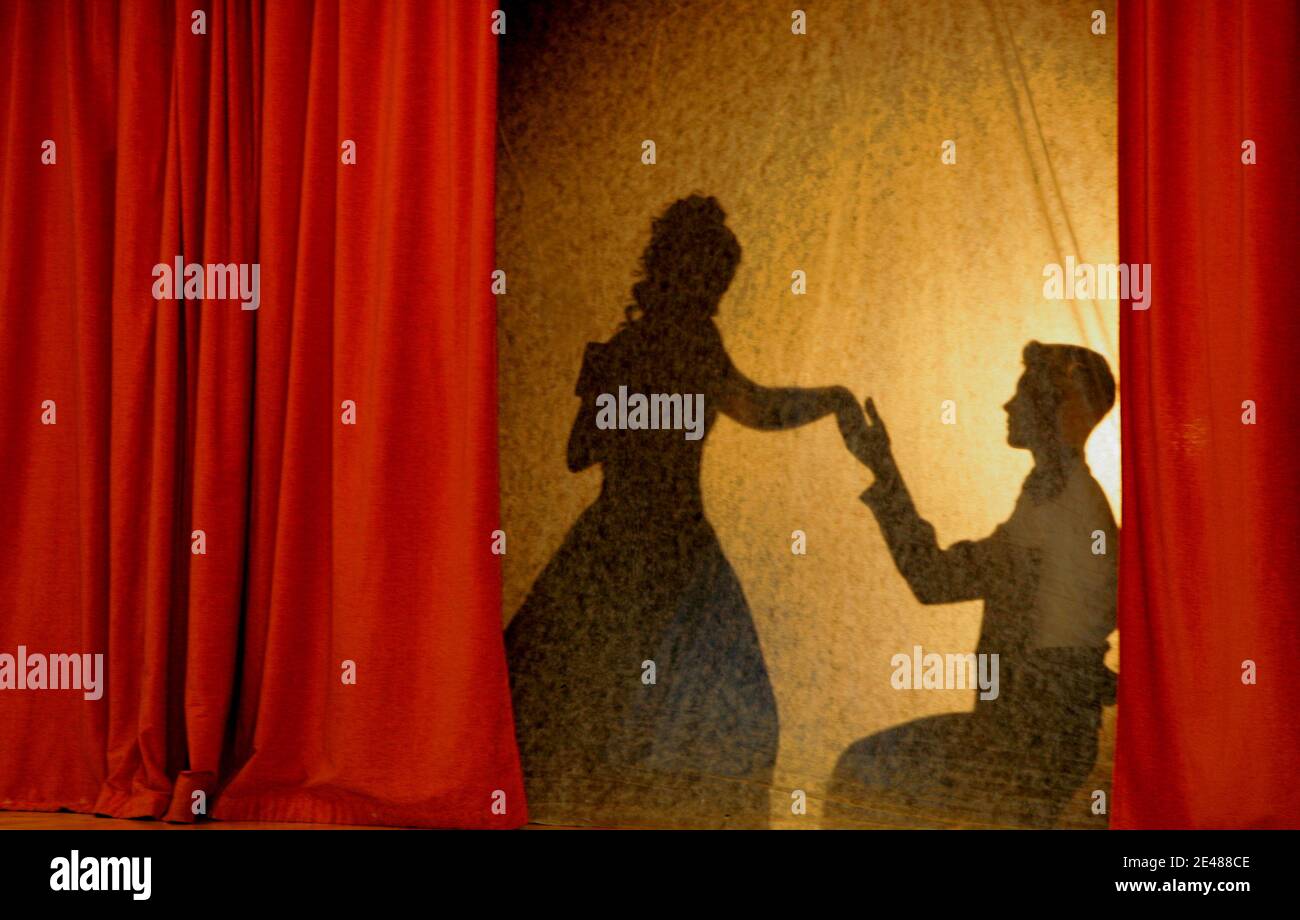 A man and woman in theatrical costumes in the theater of shadows on the stage with colored curtains. Love in the shadows theater. Stock Photo