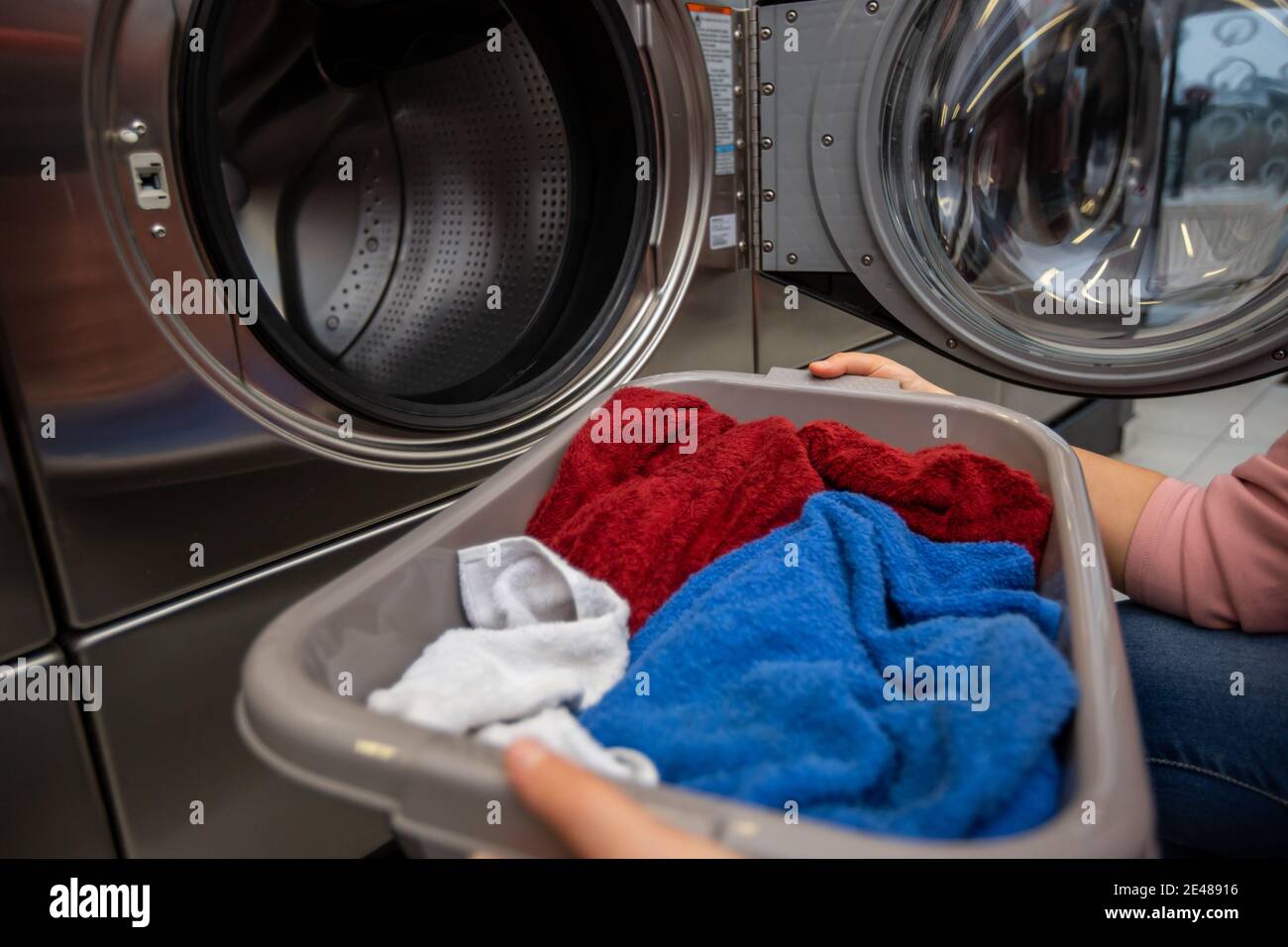 Young woman with full box of dirty clothes by the washing machine in the laundry room Stock Photo