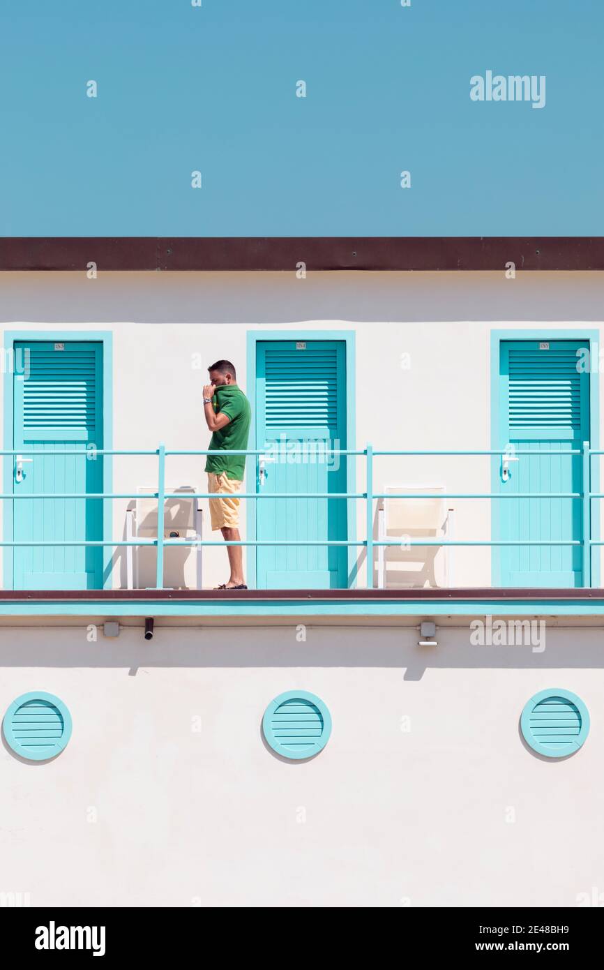 A young man undresses on a balcony in front of vintage beach cabins in Viareggio, Tuscany, Italy. Stock Photo