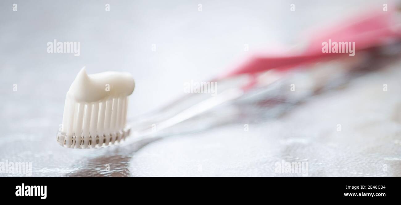 Transparent plastic toothbrush with white toothpaste on a glass table with reflection. Stock Photo