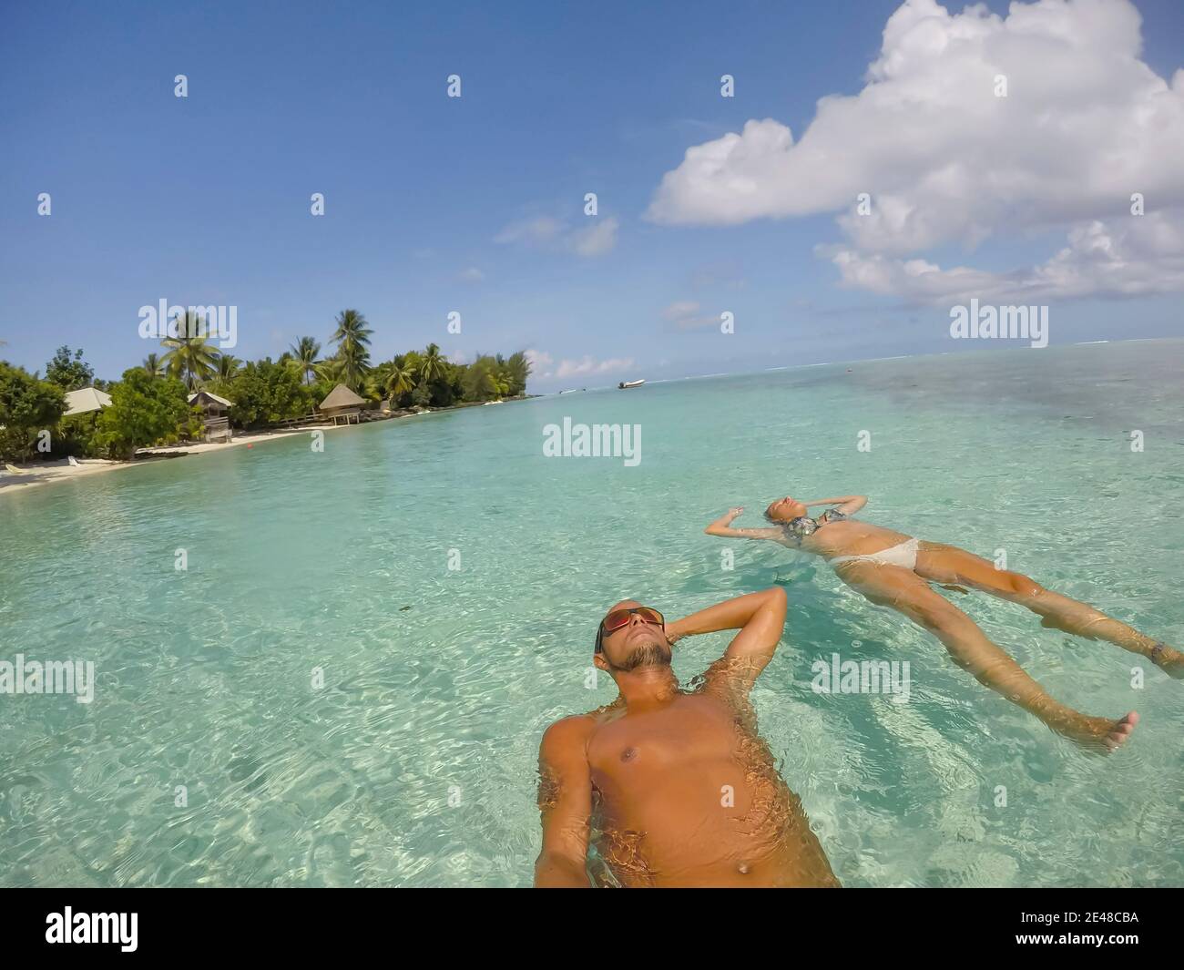 Young beautiful couple lying and floating on back in turquoise sea water on tropical paradise beach in Bora Bora Island, French Polynesia . Stock Photo
