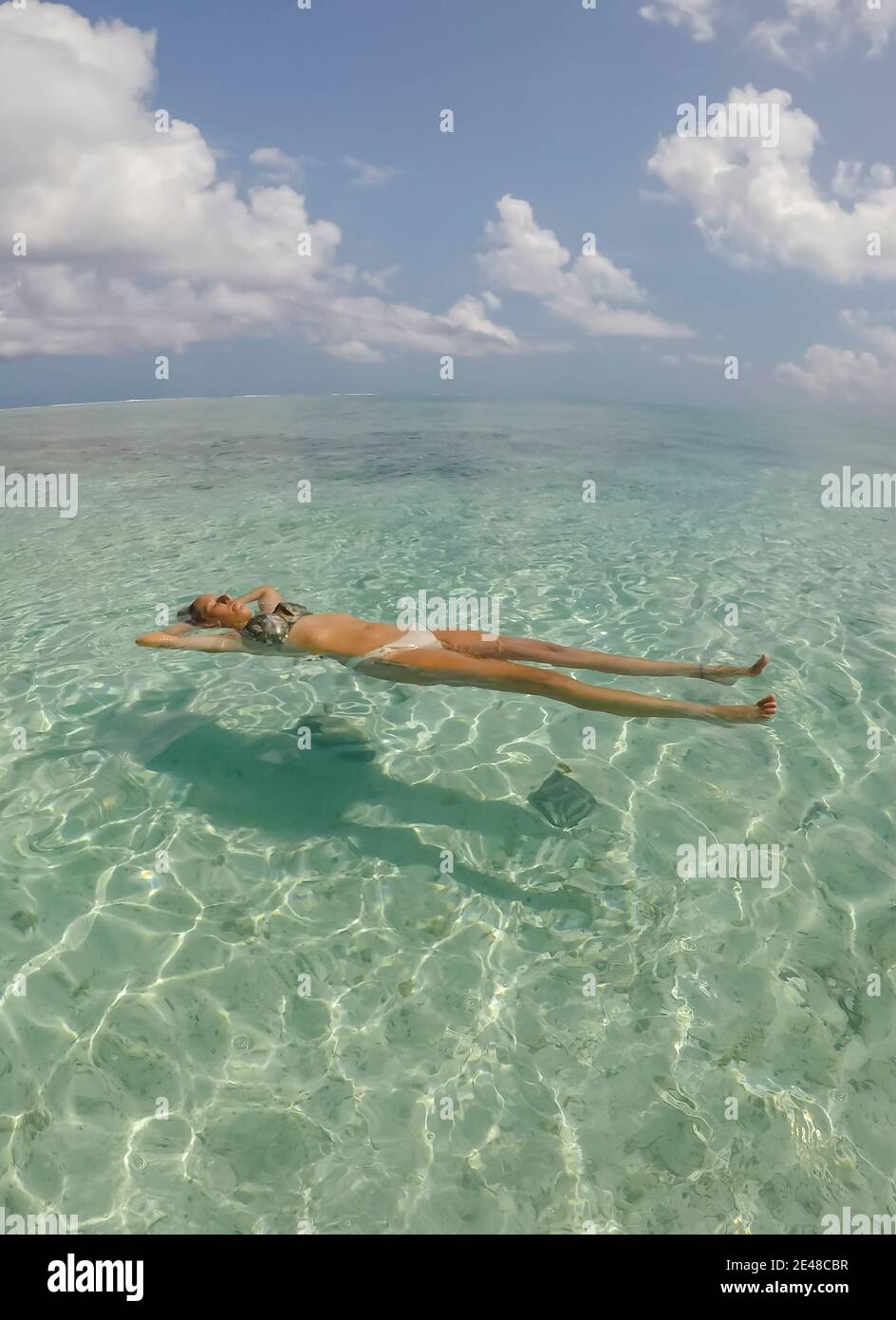 Young beautiful woman lying and floating on back in turquoise sea water on tropical paradise beach in Bora Bora Island, French Polynesia .Holidays and Stock Photo
