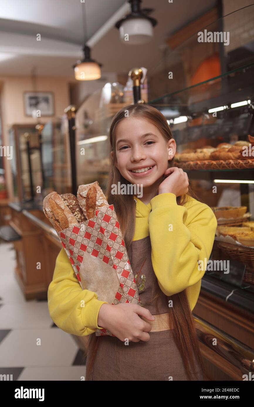 Vertical shot of a happy cute young baker girl, wearing apron, helping