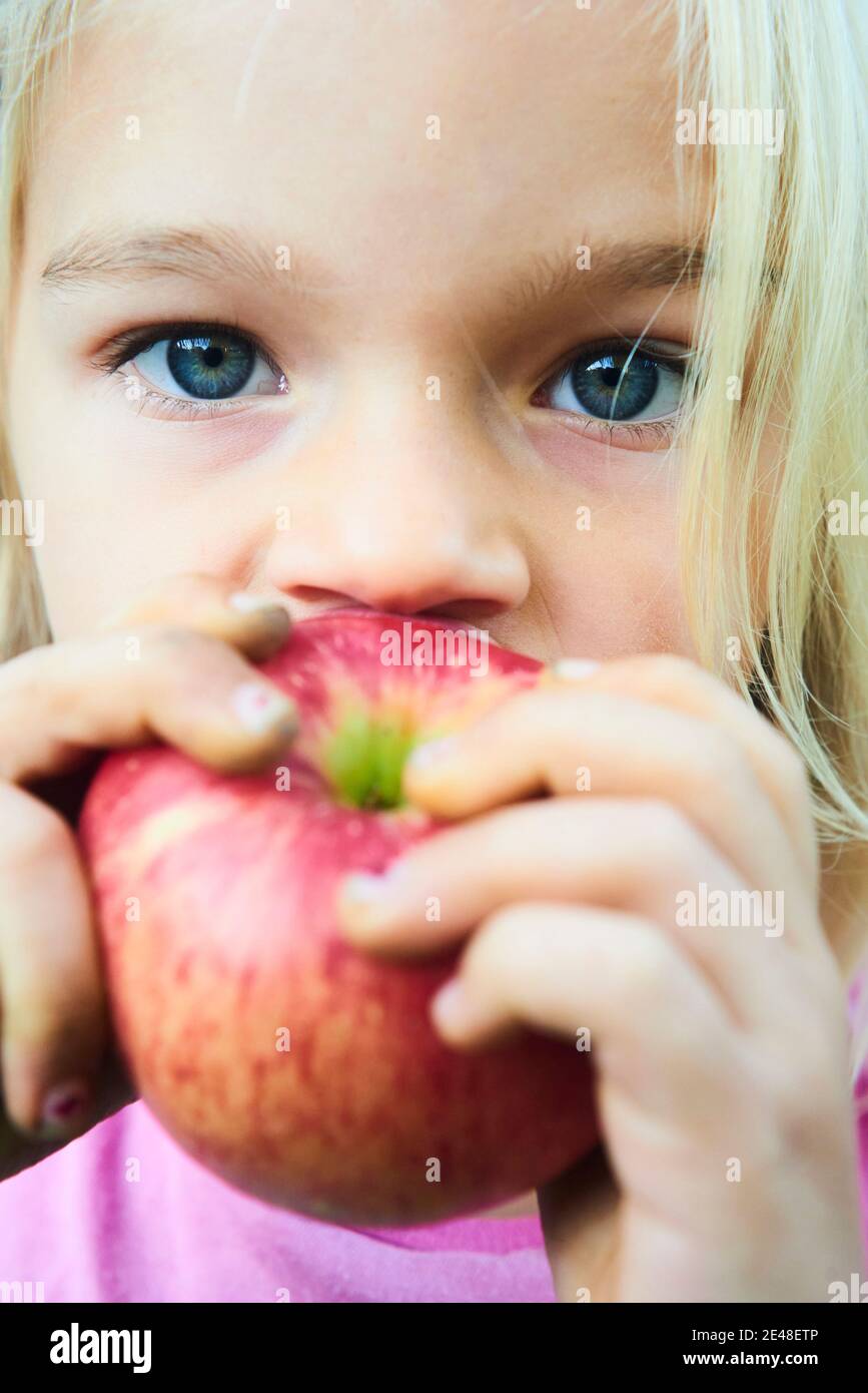 Child girl eating fresh apple after plucking from the tree. Closeup portrait Stock Photo