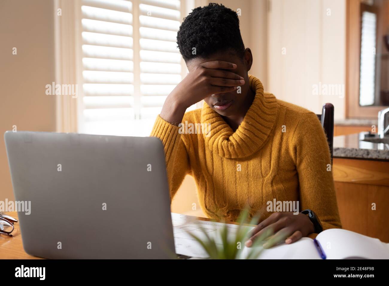 African american woman using laptop rubbing her eyes in kitchen Stock Photo