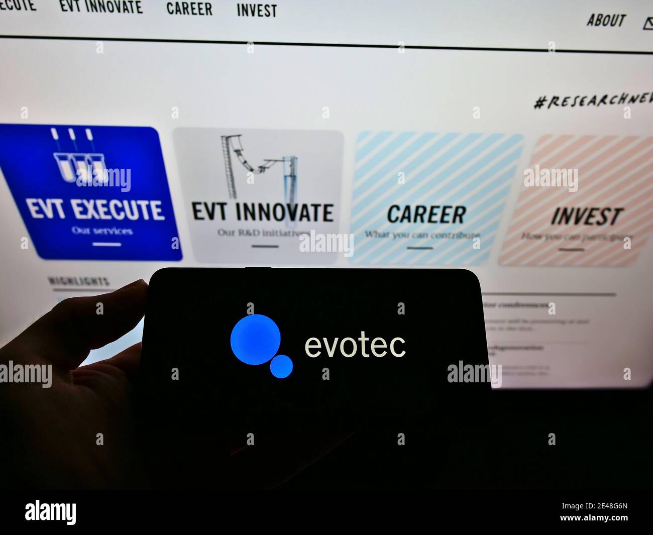 Person holding smartphone with business logo of German biotechnology company Evotec AG on display in front of website. Focus on mobile phone screen. Stock Photo