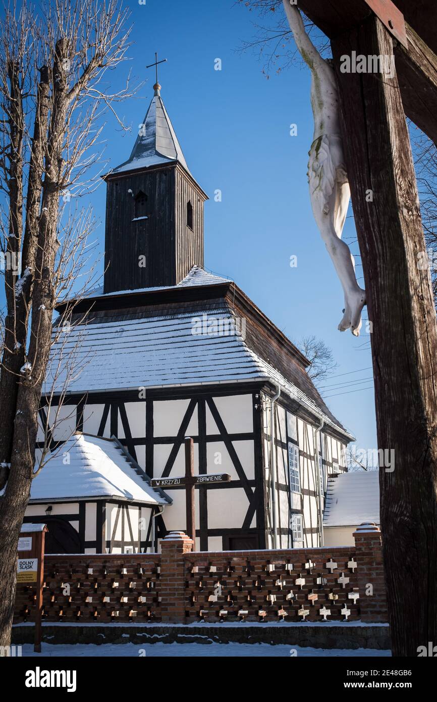 Wooden Catholic church and Crucyfix on the first plan. Subtitles in Polish on crucyfix: Salvation in the crucyfix, and bottom name of region of Poland Stock Photo