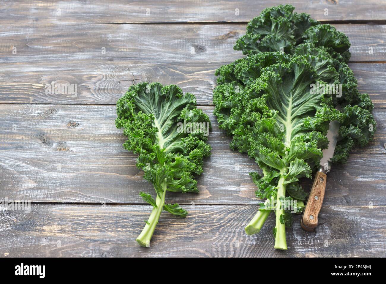 Fresh green curly kale leaves on a cutting board on a wooden table. selective focus. free space. rustic style. healthy vegetarian food Stock Photo