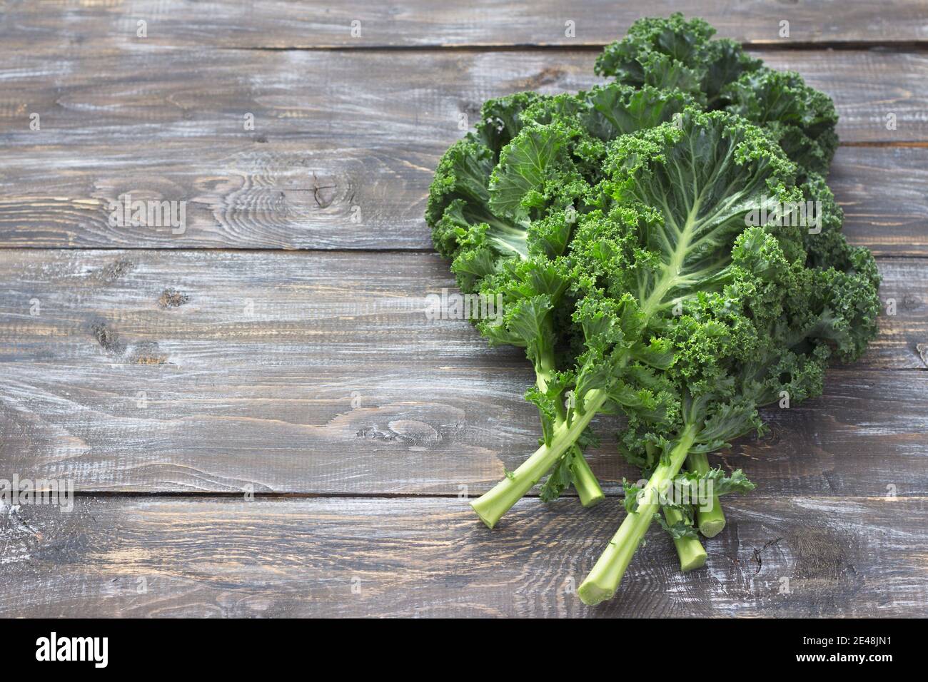 Fresh green curly kale leaves on a cutting board on a wooden table. selective focus. free space. rustic style. healthy vegetarian food Stock Photo