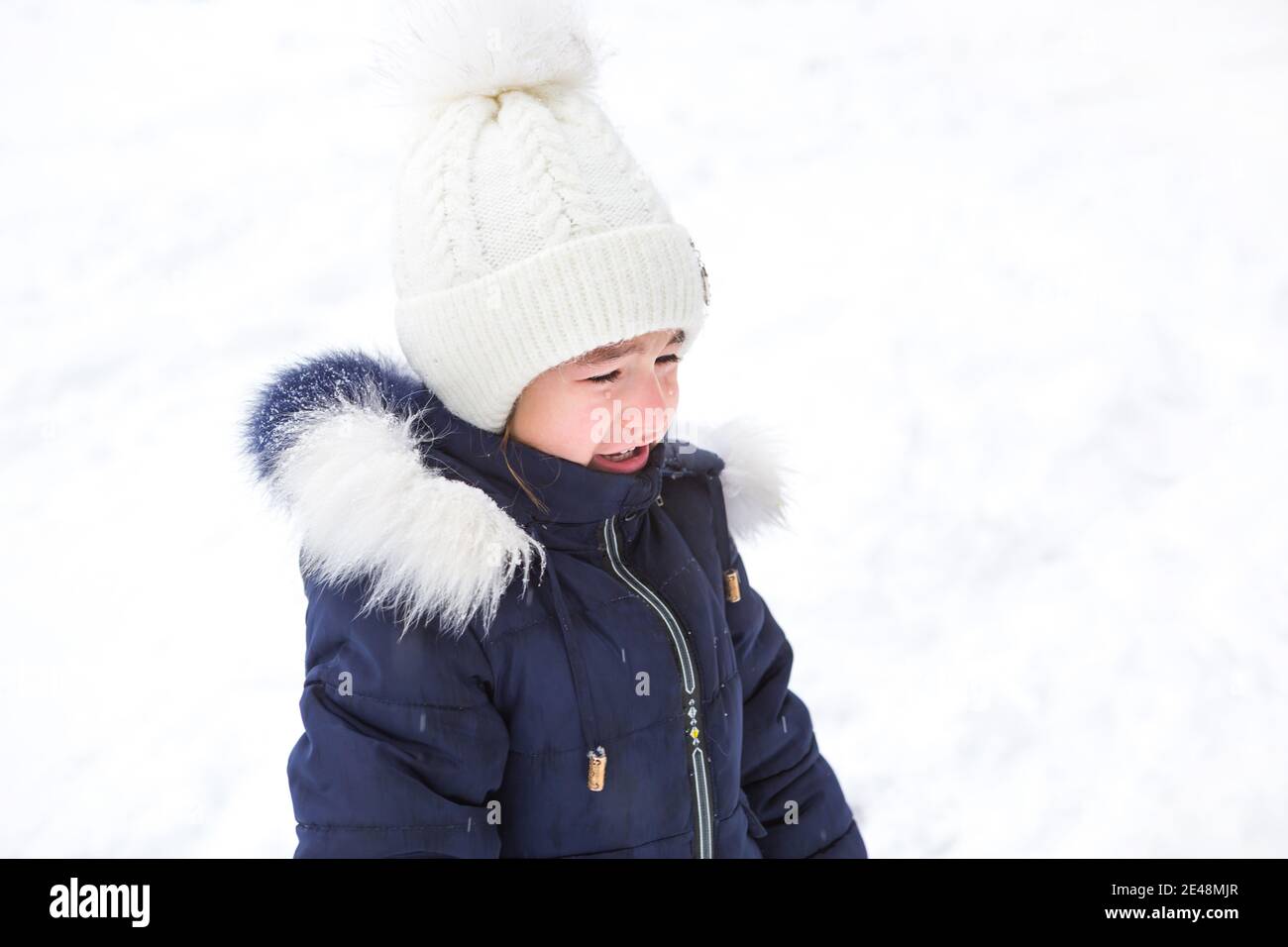Little girl crying outside in winter. A child in warm clothes is upset, cold, wipes away tears, screams, is capricious and hysterical. Winter, snow, f Stock Photo