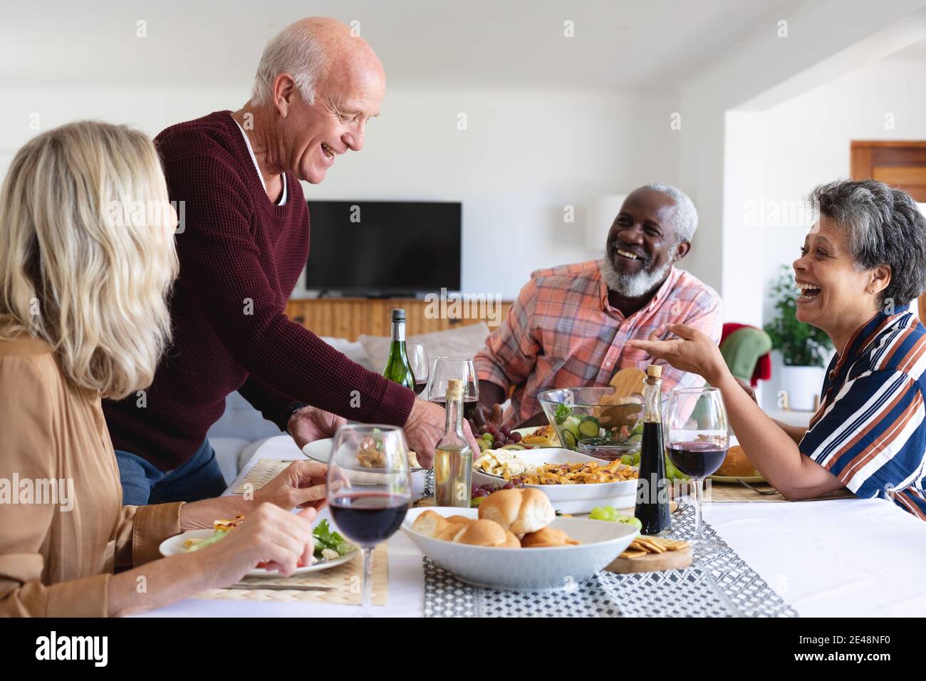 Senior caucasian and african american couples sitting by table eating dinner at home Stock Photo