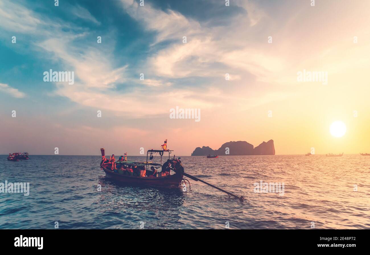 Thailand ocean boats cruise: people traveling on water transport at sun setting tones. Majestic sunset tourist vacation at waterfront. Mountain island silhouette at skyline under cloudy sky Stock Photo