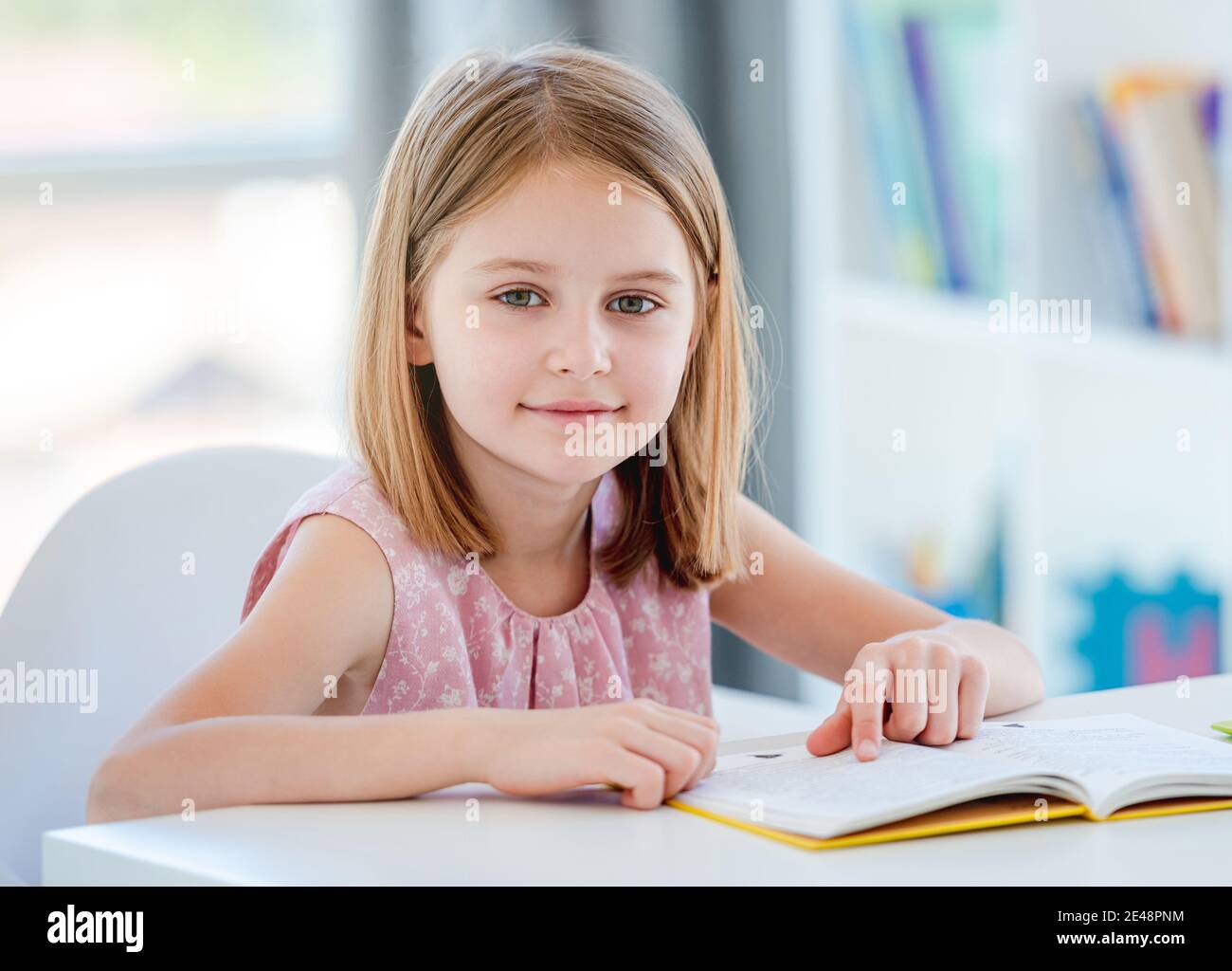 Schoolgirl with textbook sitting at desk Stock Photo - Alamy