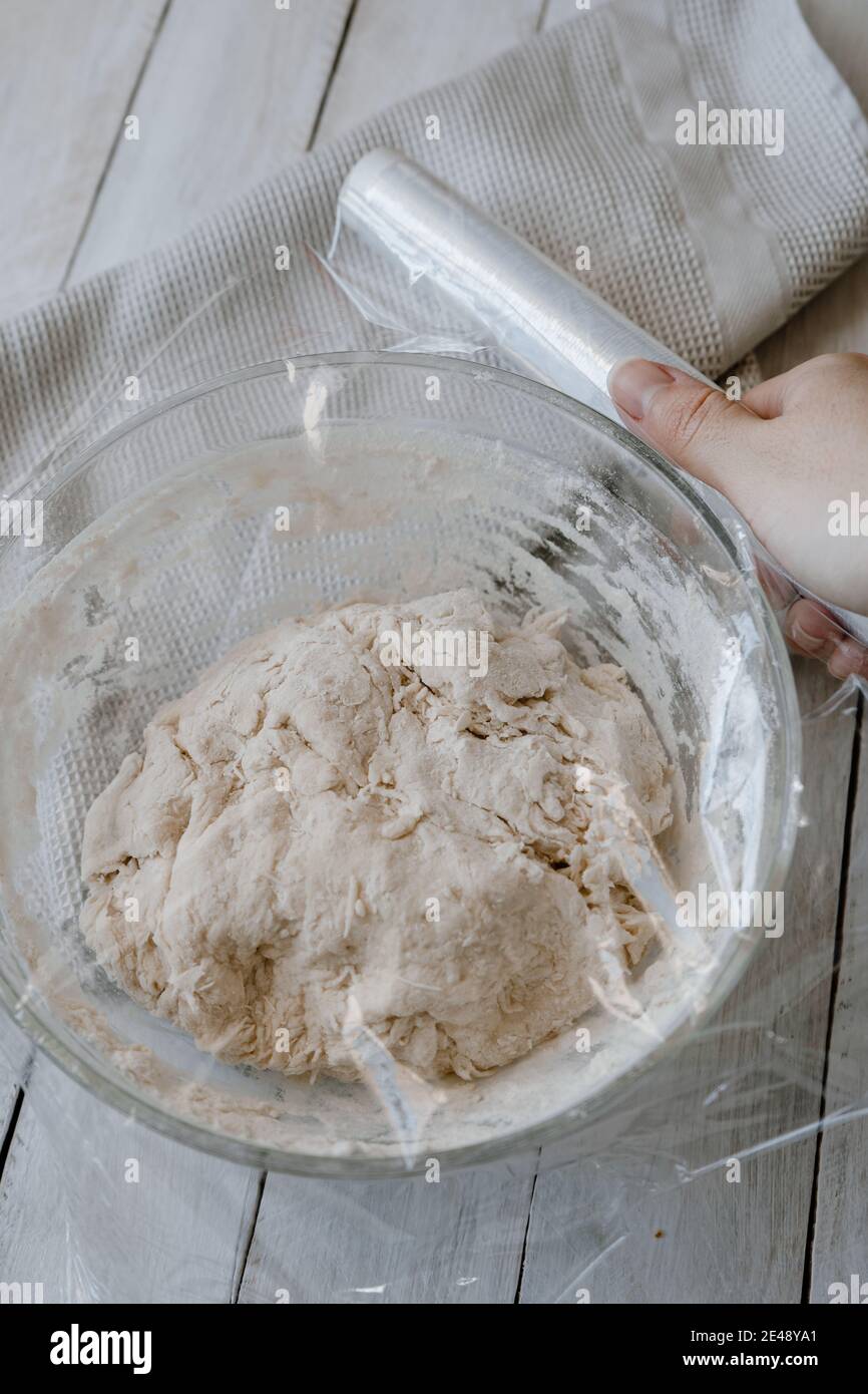https://c8.alamy.com/comp/2E48YA1/hand-covering-with-plastic-wrap-a-bowl-with-homemade-no-knead-bread-dough-2E48YA1.jpg