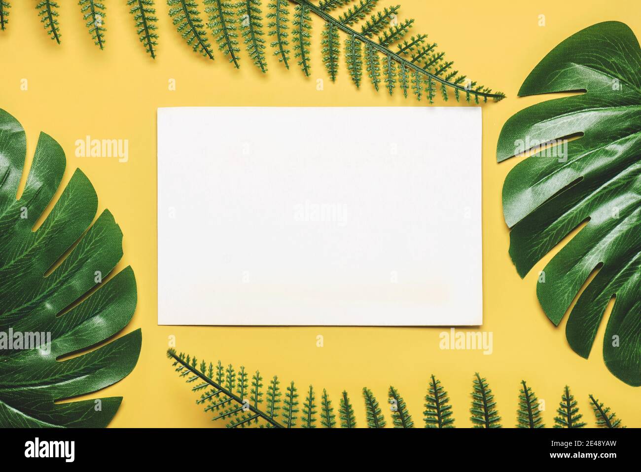 Tropical palm leaves frame with white paper in the center on yellow ...