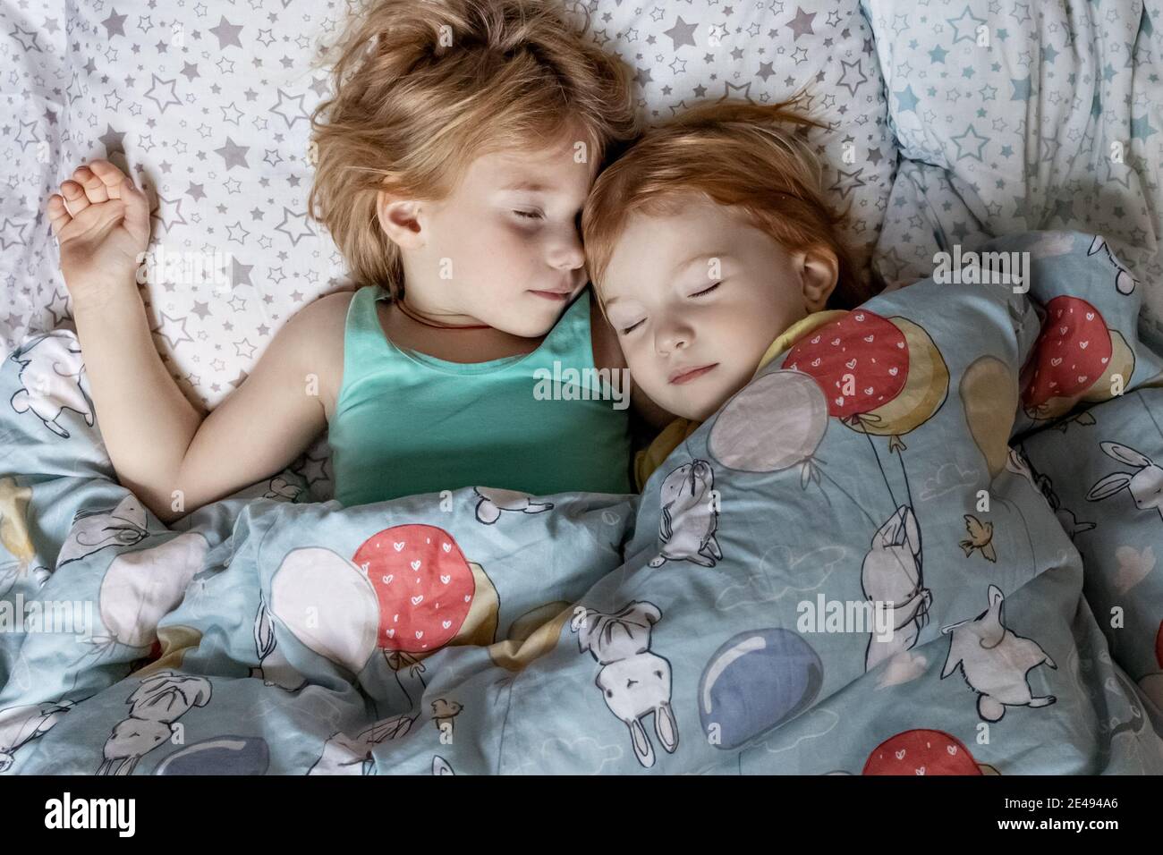 Two little sibling girls sisters sleeping in an embrace in bed under one blanket. Stock Photo