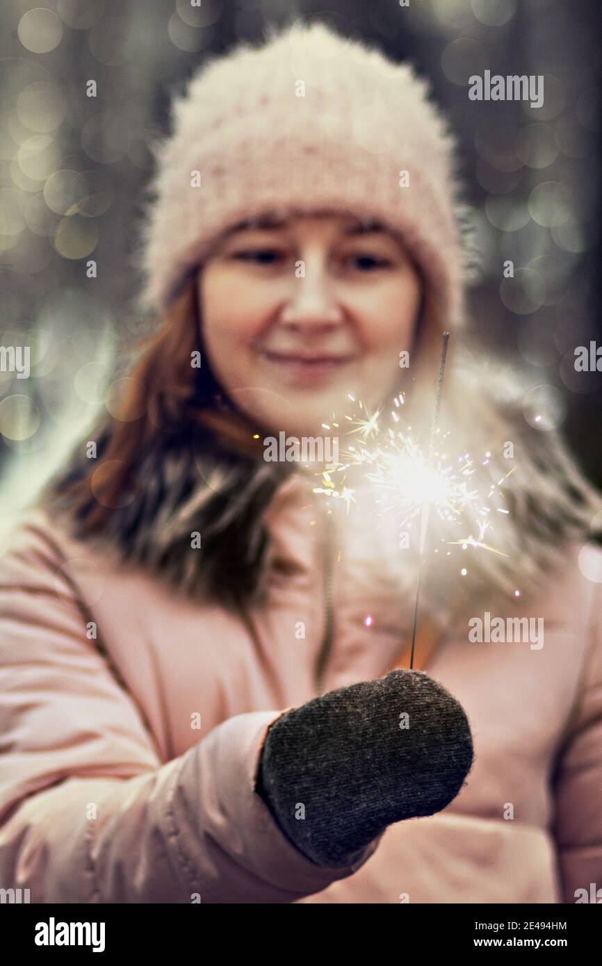 Christmas lights are bright splashes burning in the hands of a blurry happy woman in the park. Sparkler. Emotions, New Year's mood.Winter holidays. Stock Photo