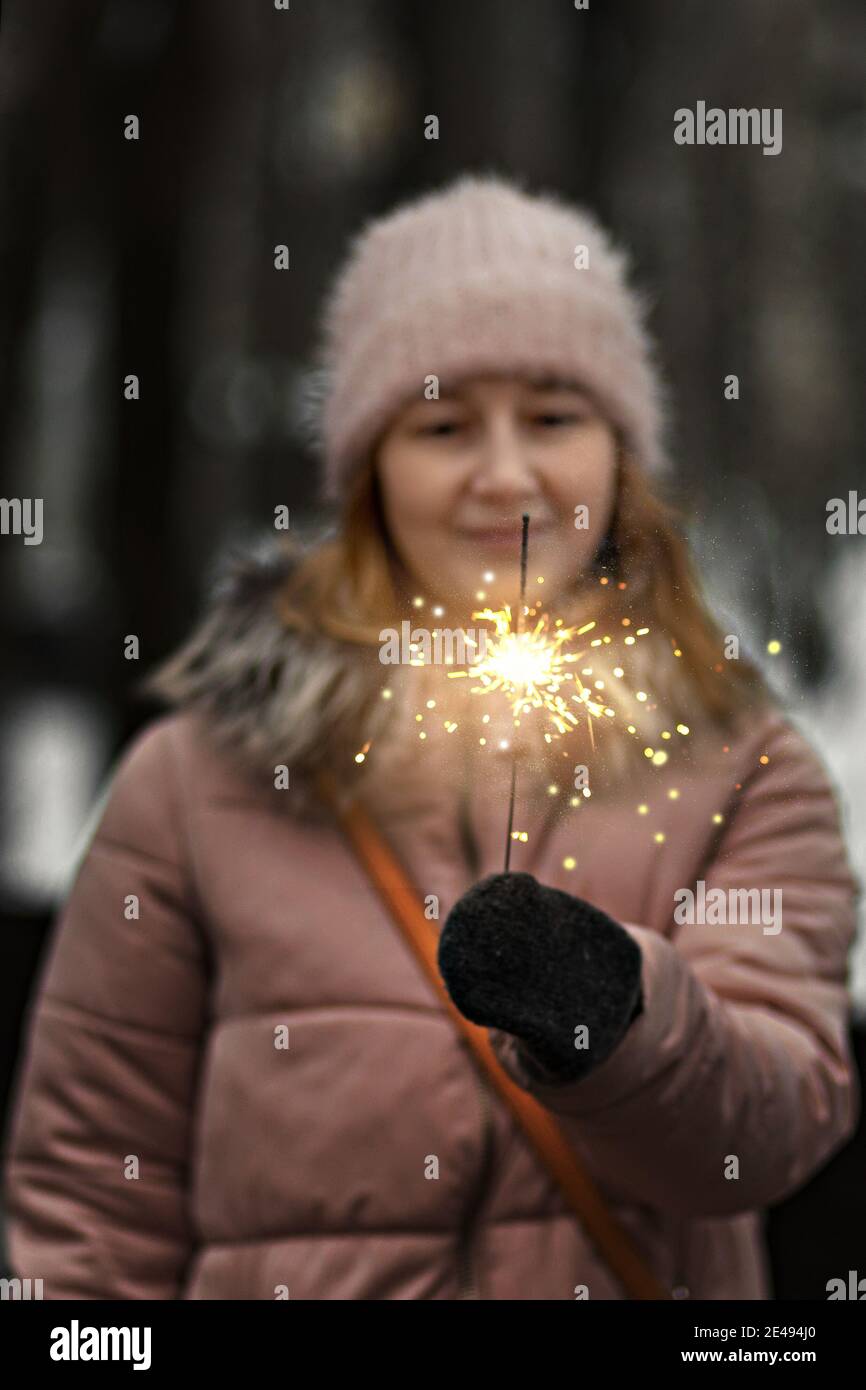 Christmas lights are bright splashes burning in the hands of a blurry happy woman in the park. Sparkler. Emotions, New Year's mood.Winter holidays. Stock Photo