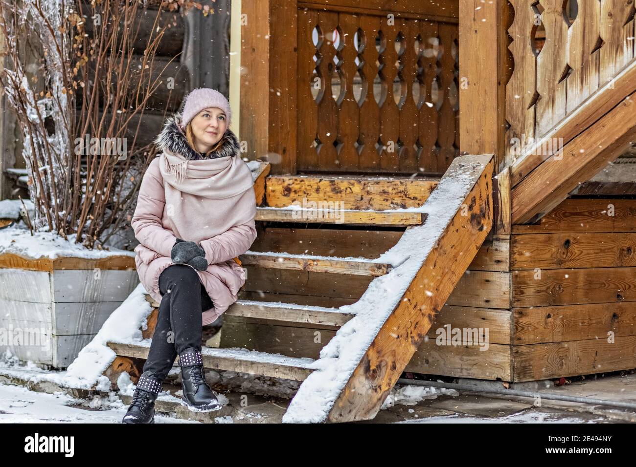 Warmly dressed young woman posing on the porch of a wooden house in the ...