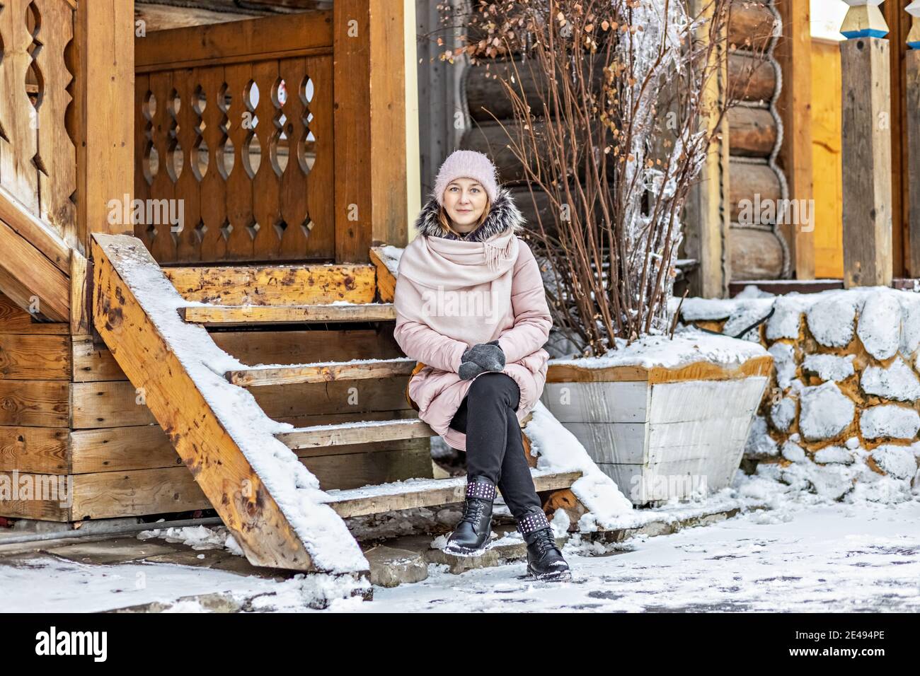 Warmly dressed young woman posing on the porch of a wooden house in the ...