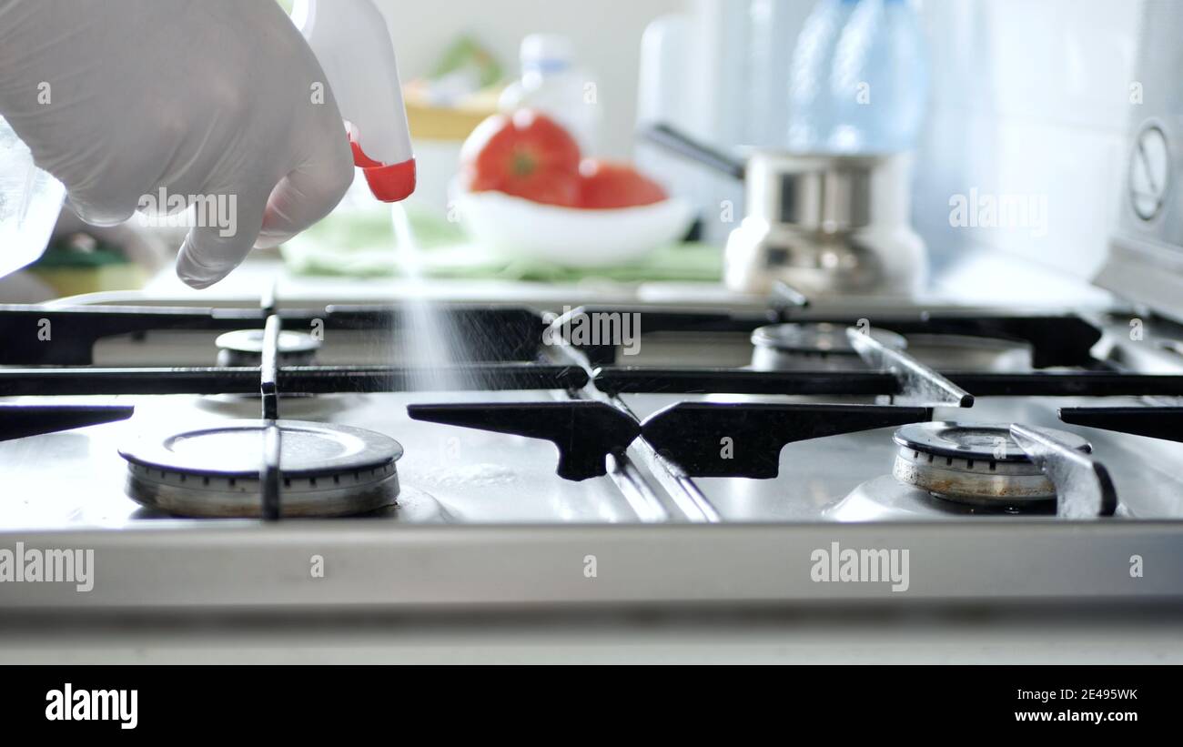 Busy Person in the Kitchen Wearing Gloves Cleans with Solution the Cooker Stove. Stock Photo