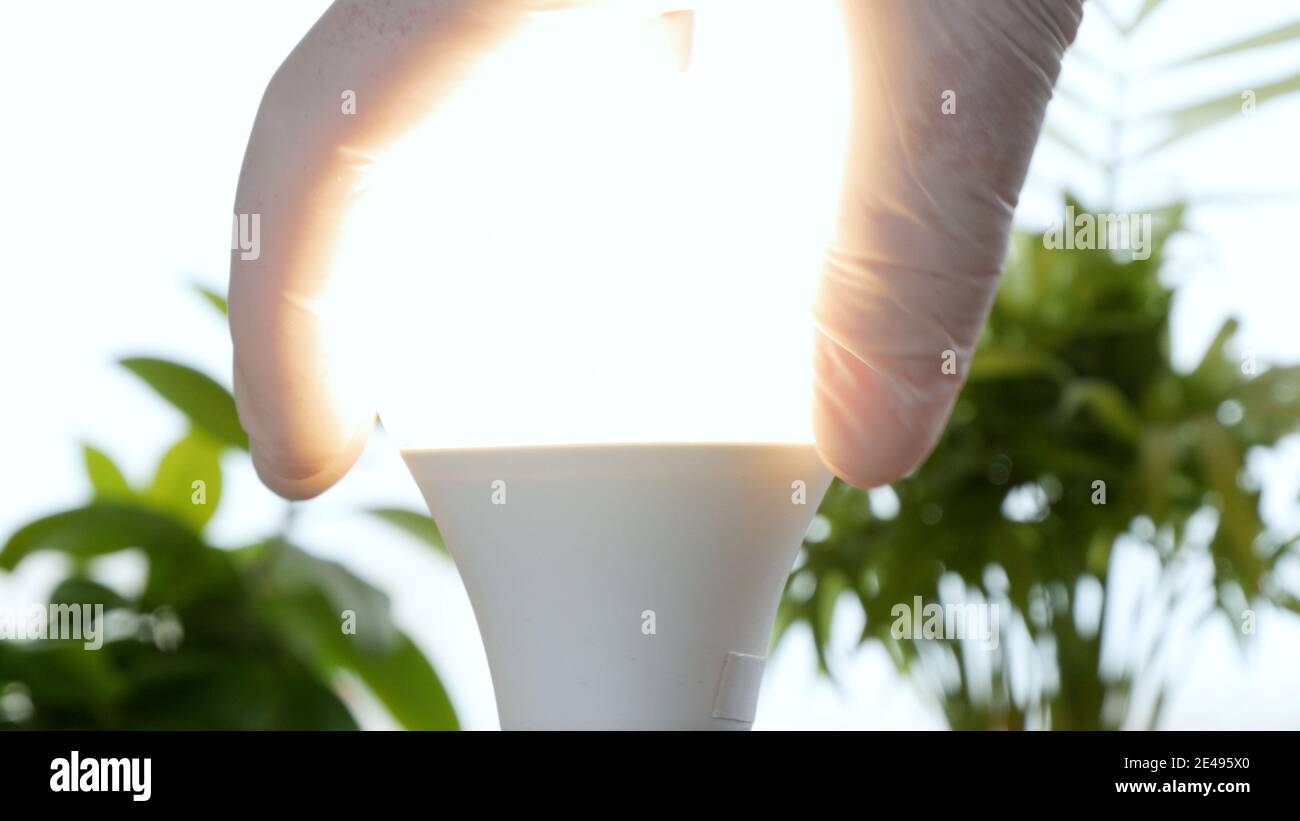 Electrician's Hand Rotates a Led Bulb in Electrical Socket Turning On the Light Stock Photo