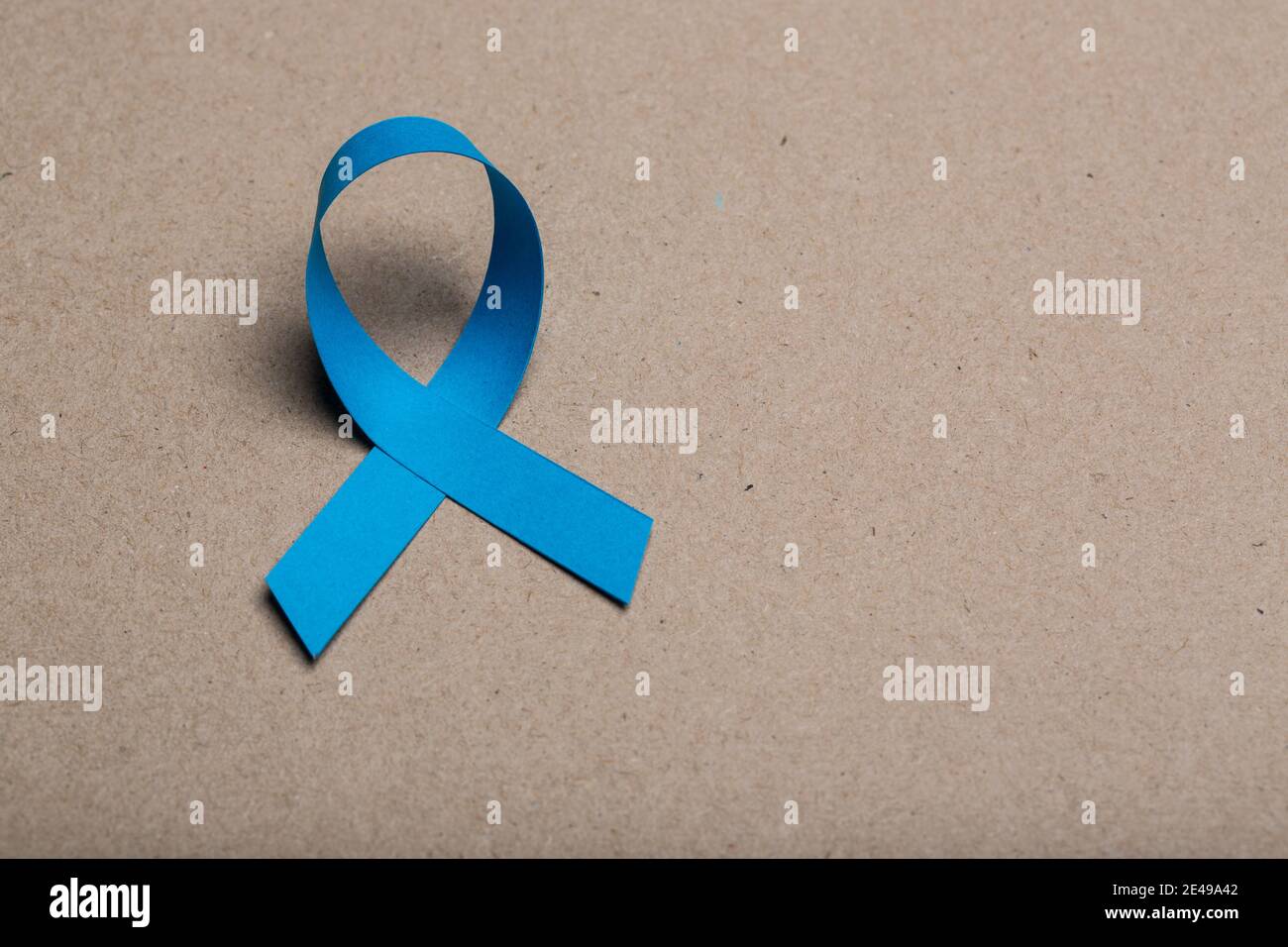 Blue handmade awareness paper ribbon on cardboard background. Stock Photo